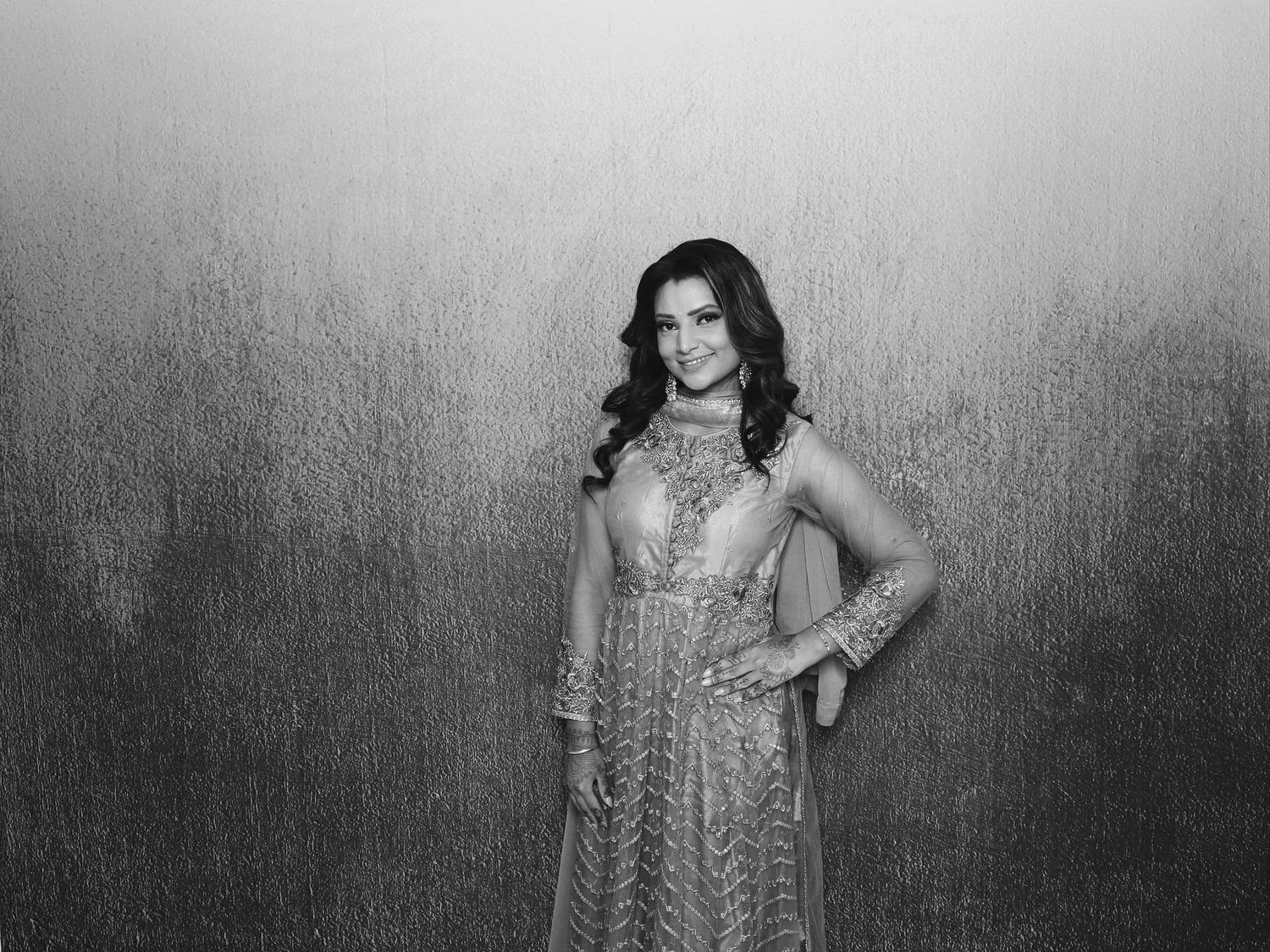 Woman in elegant embroidered Indian anarkali dress poses confidently in black and white photo.