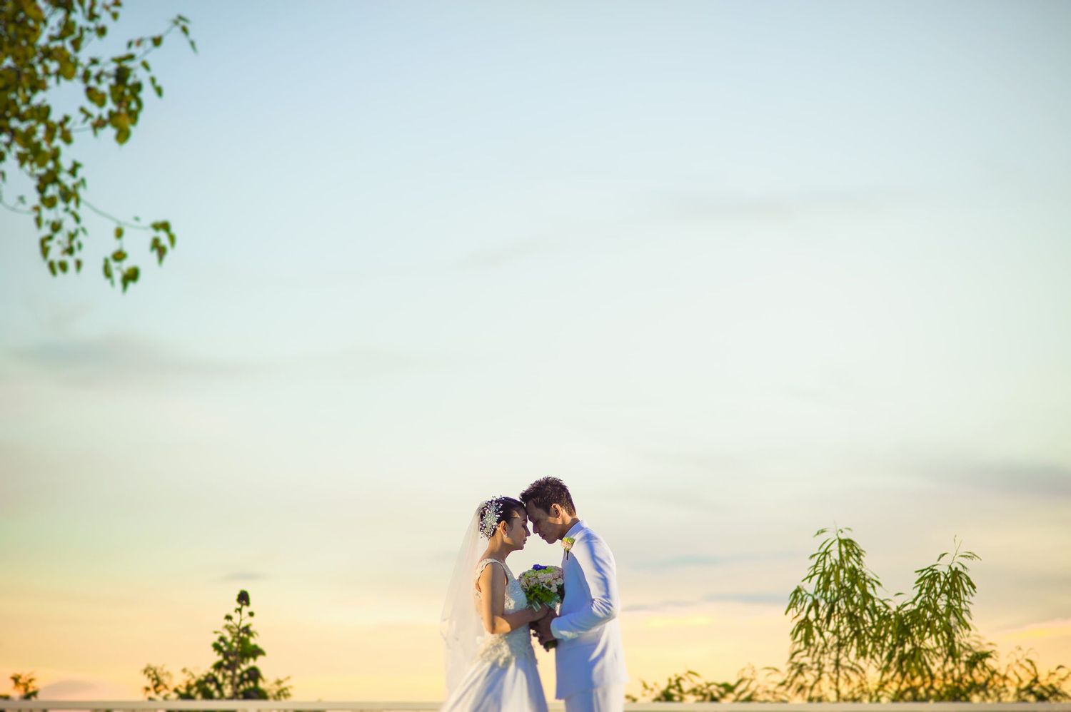 A couple shares a romantic embrace at sunset during their outdoor wedding ceremony, bride holding a bouquet.