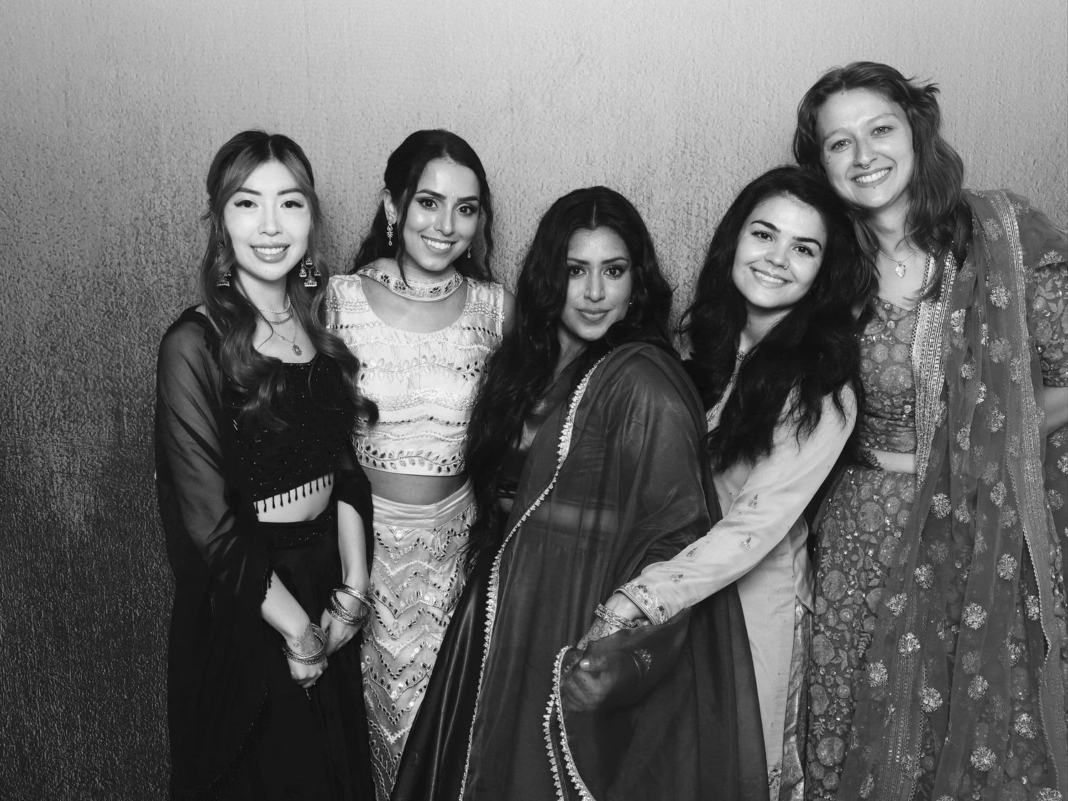 Five women pose together in elegant traditional attire at a formal event in this black and white photo.