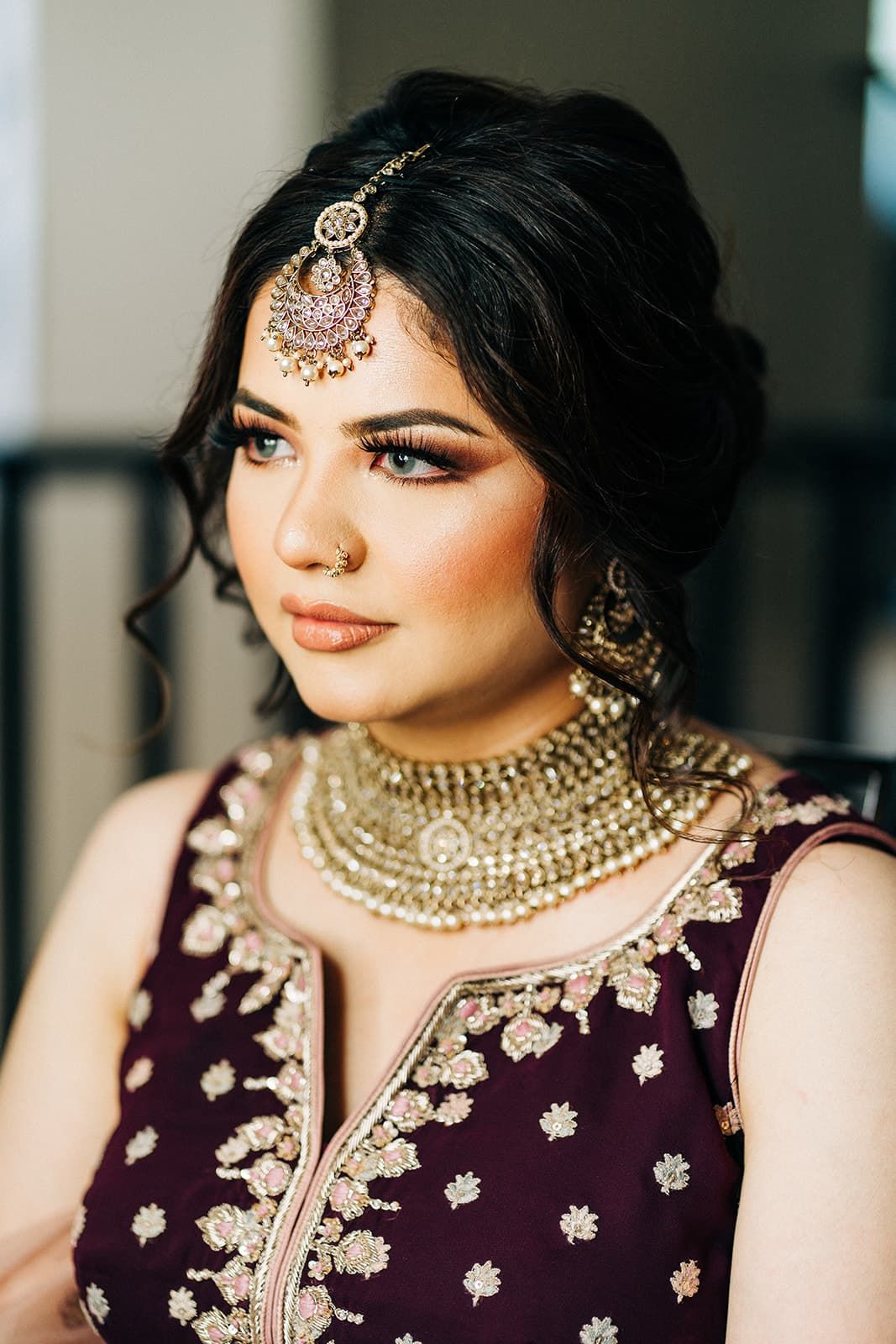Indian bride wearing gold maang tikka, chandbali earrings, and kundan choker in deep purple lehenga.