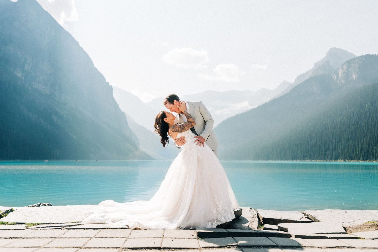 Bride and groom share a romantic kiss by turquoise Lake Louise with majestic mountain backdrop on their wedding day.