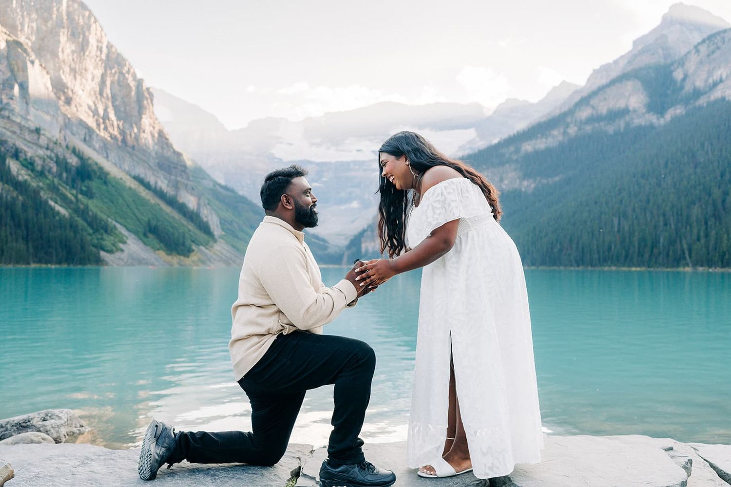 Man proposing to woman on one knee by turquoise glacial lake with mountain backdrop in Banff, Canada.