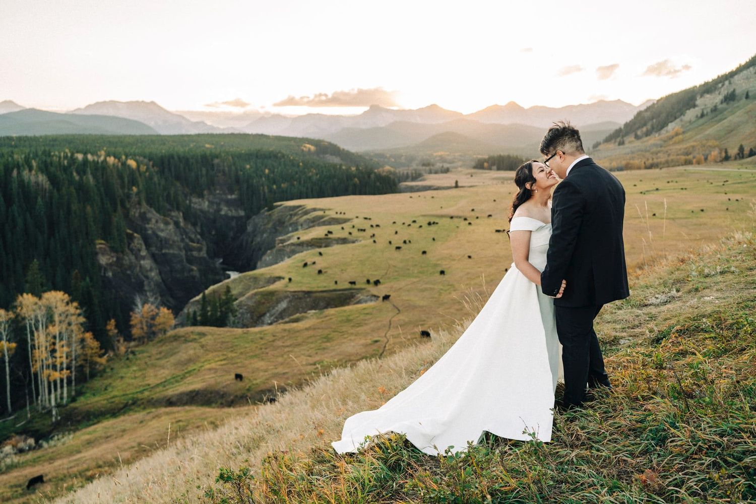 Bride and groom share a romantic kiss on a scenic mountain overlook during golden hour at their outdoor wedding.