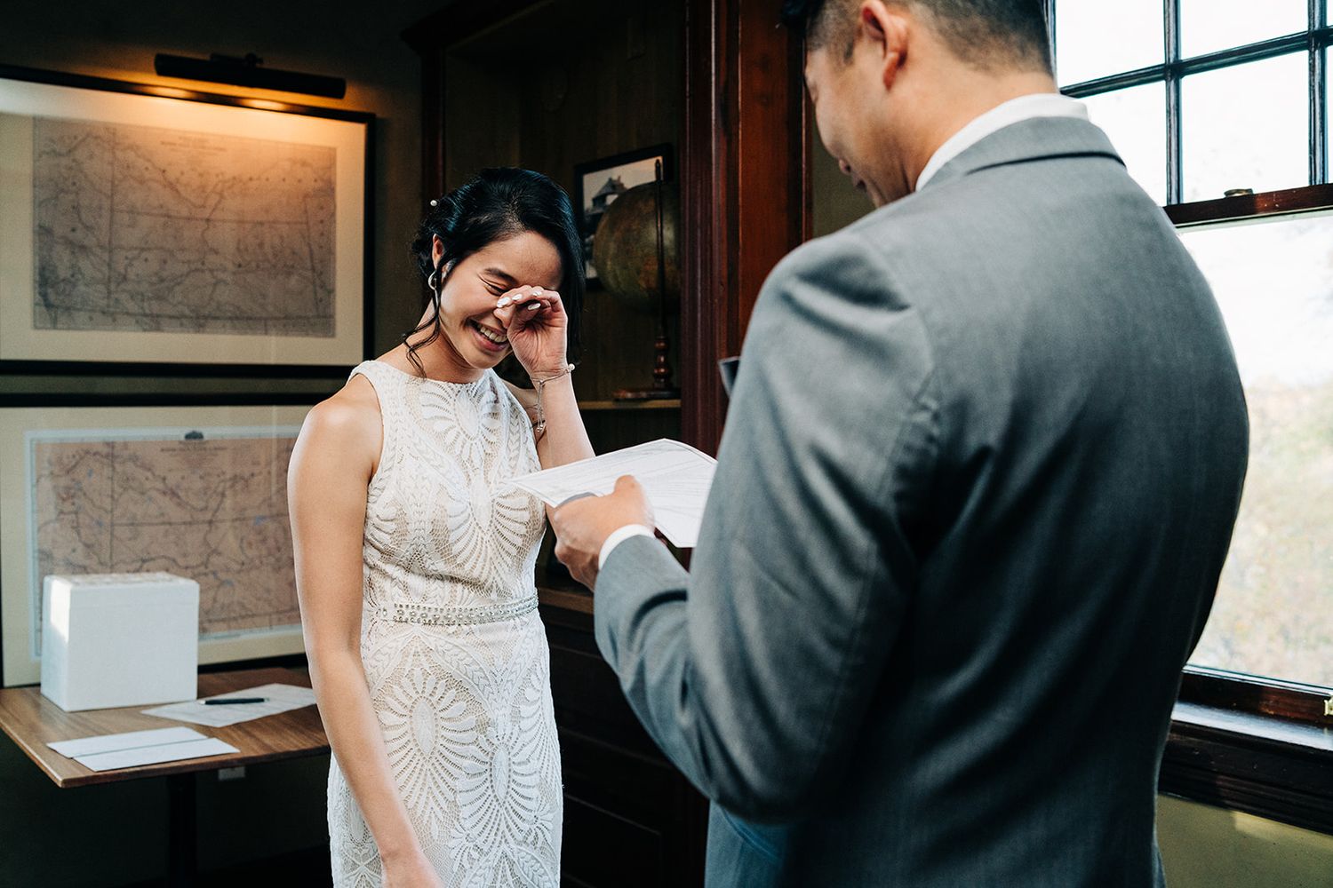 An emotional wedding ceremony moment in a room with wooden interior and window lighting.