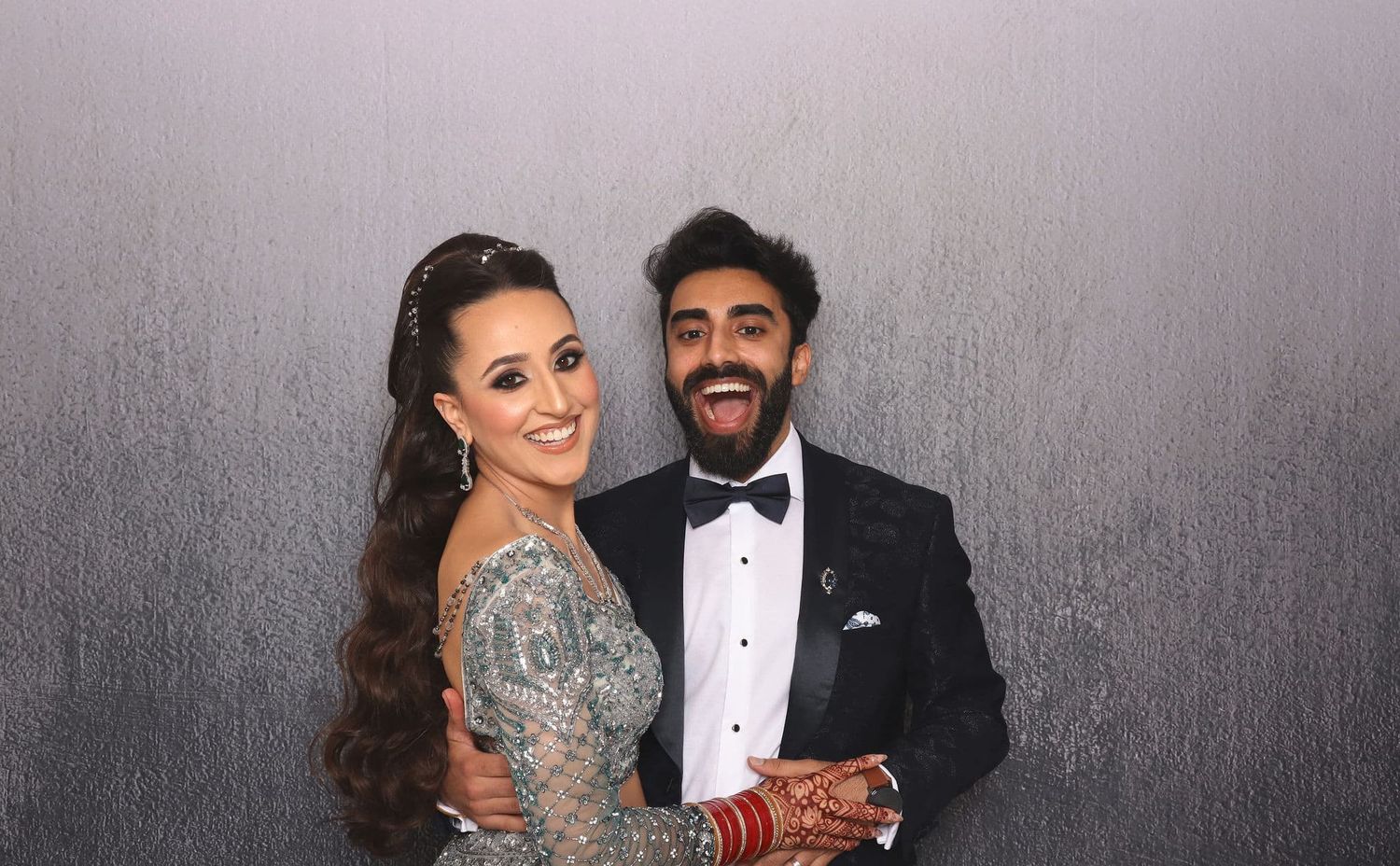 Couple in formal attire smiling at camera, woman in embellished gown and man in tuxedo, photo booth style portrait.
