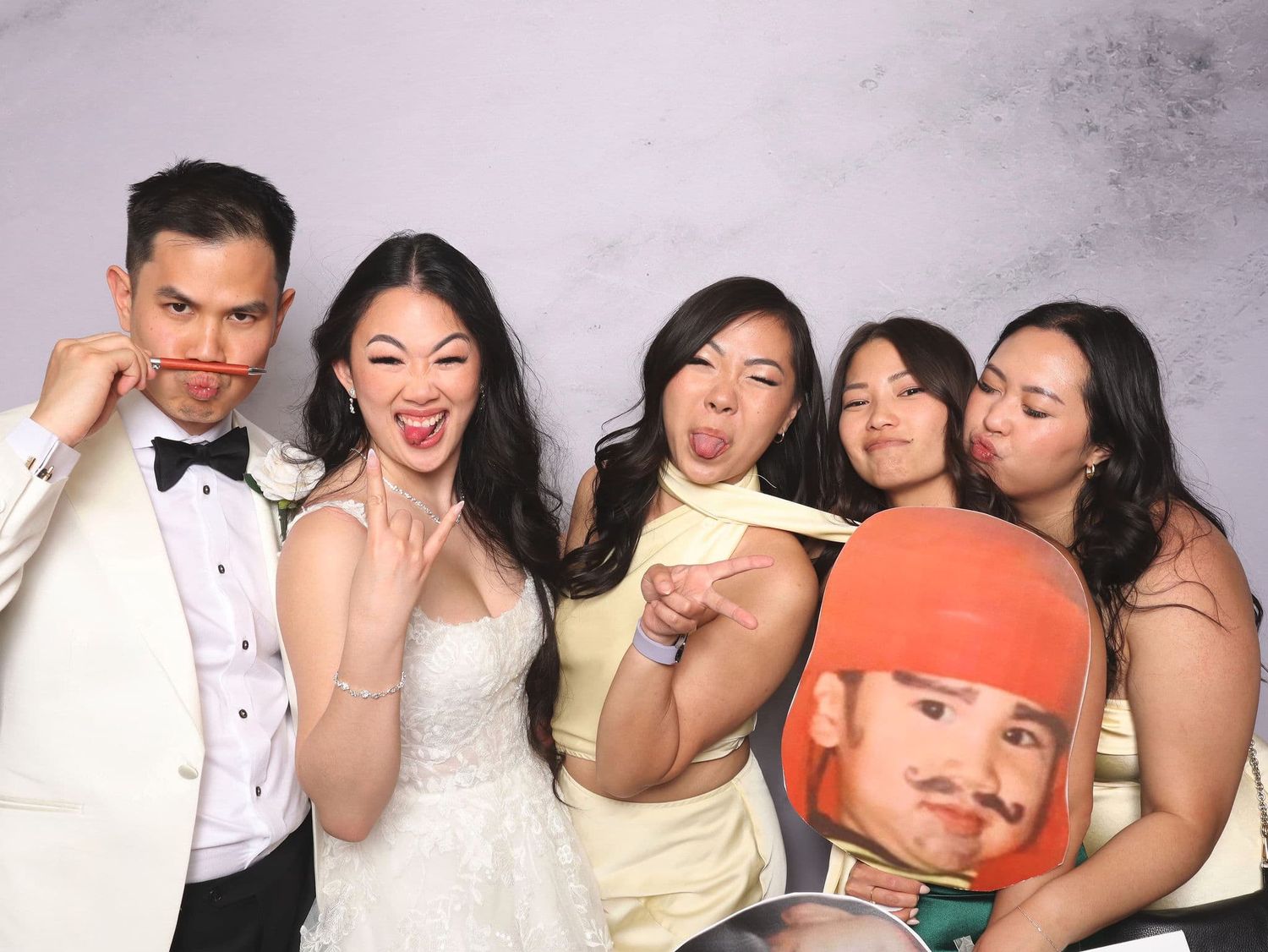 Wedding party of five posing playfully in photo booth, bride in white gown with friends.
