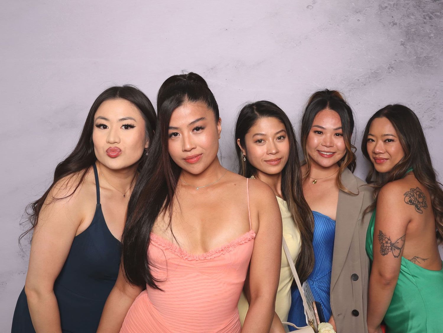 Five young women in colorful dresses smile together in a vibrant photo booth picture.