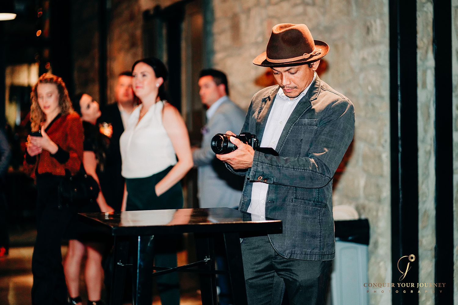 A group of people gathered at a social event, with some holding cameras and drinks in a warm-lit indoor setting.