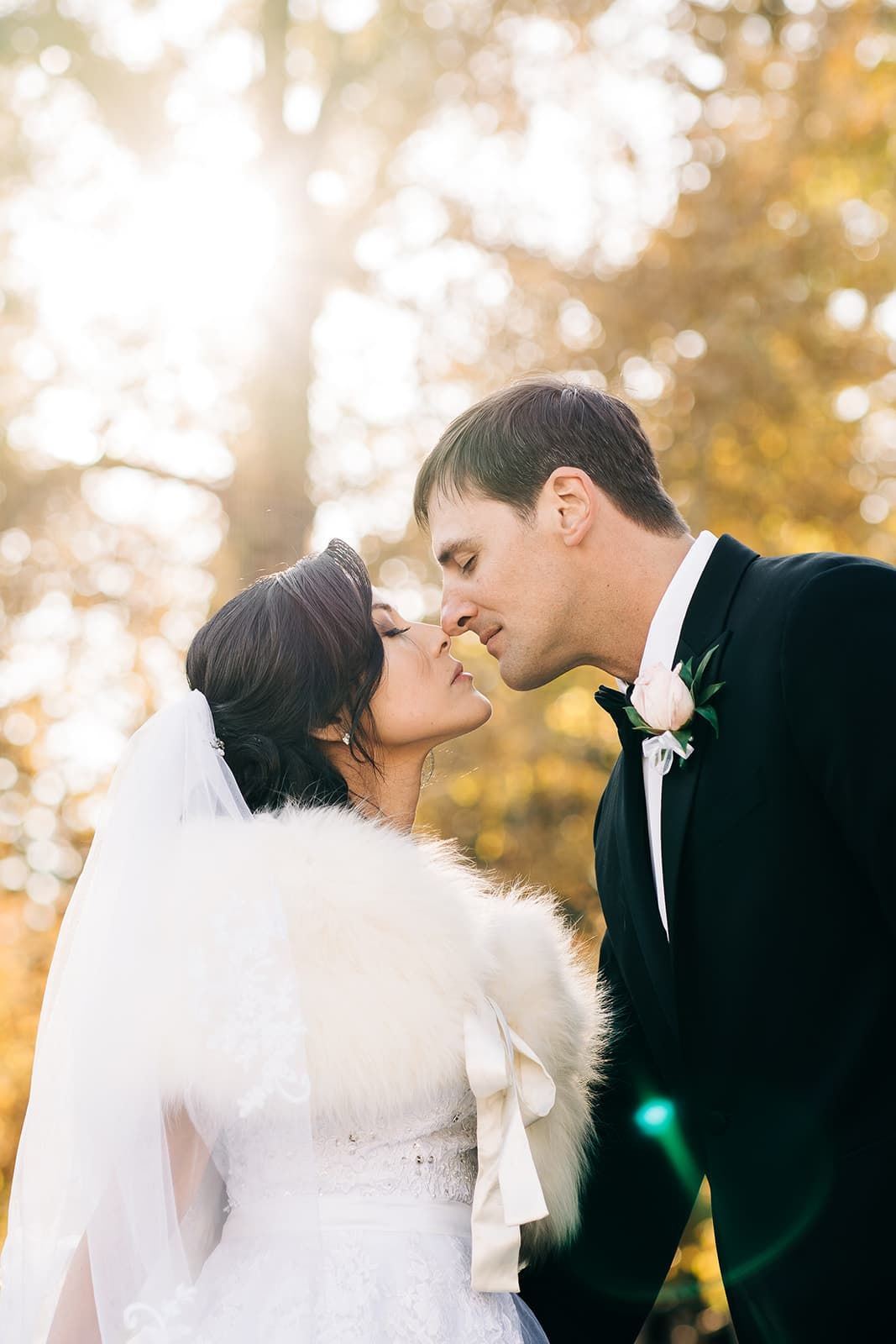 Bride and groom sharing a romantic kiss in golden autumn sunlight in a forest setting.