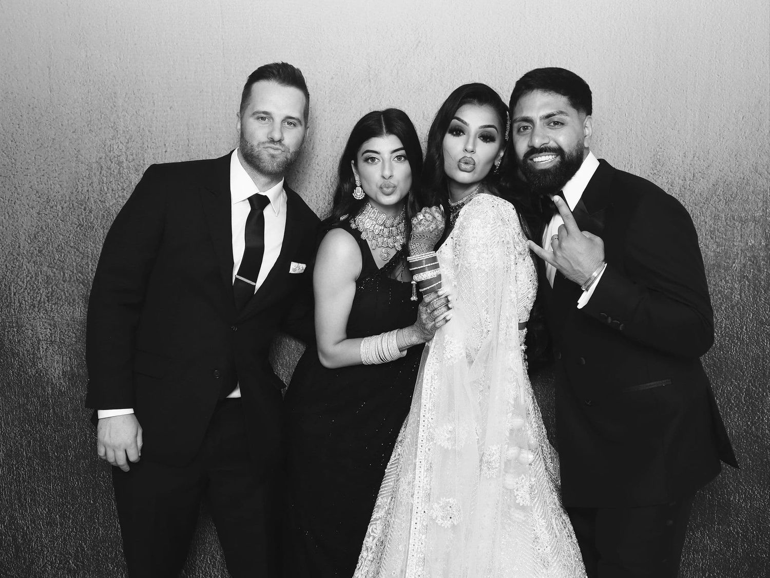 Two couples pose together at a formal wedding event in elegant black and white attire.