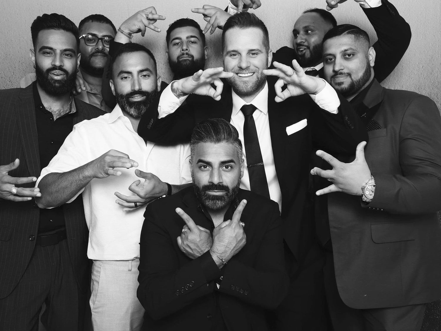 Group of eight men posing together in black and white photo booth picture at a formal event.