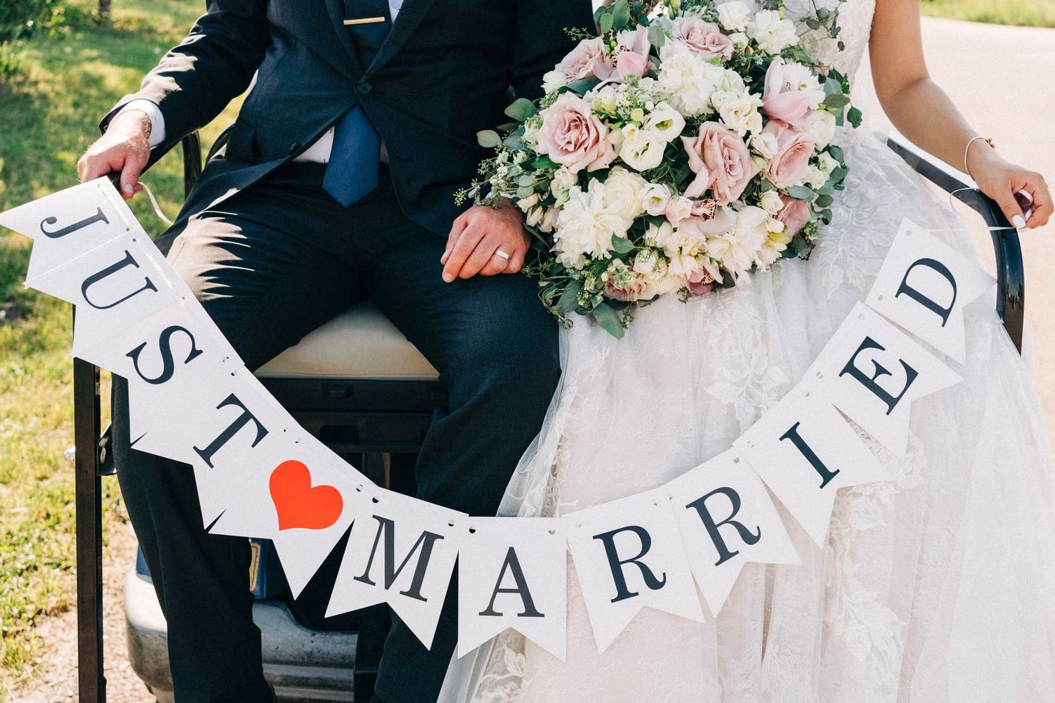 Newlyweds hold a Just Married banner sign at their outdoor wedding ceremony celebration.