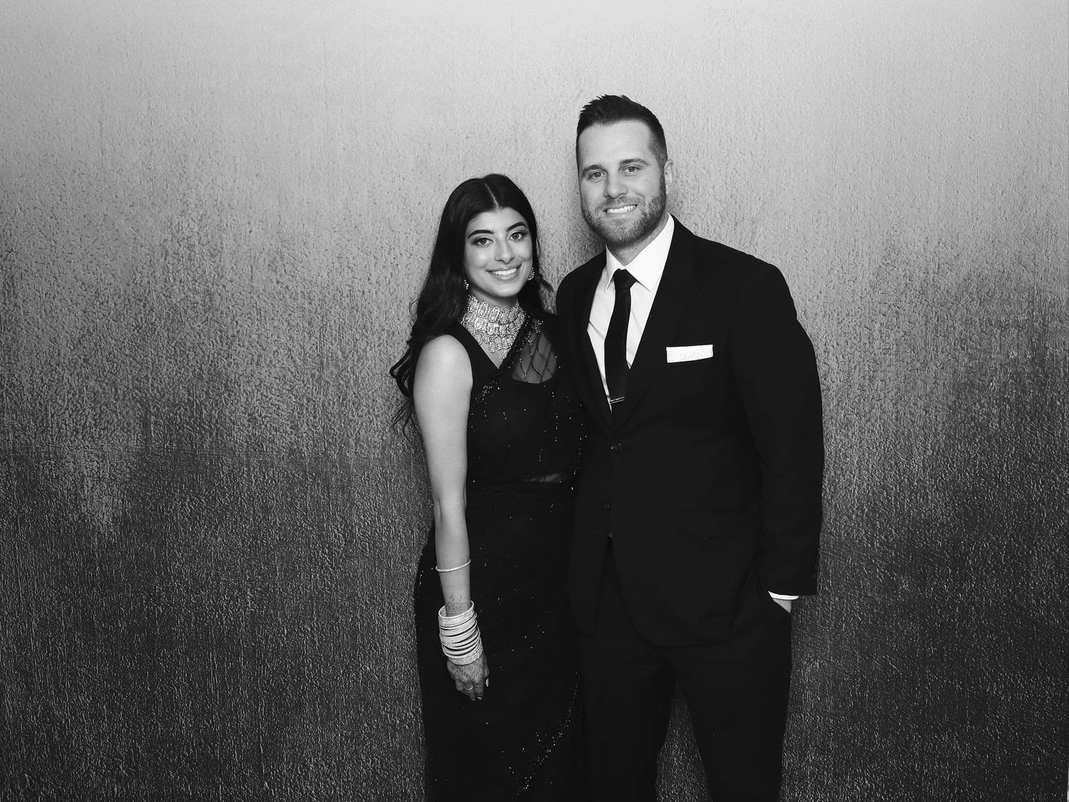 A couple poses together in black and white, dressed in formal attire at an elegant event.