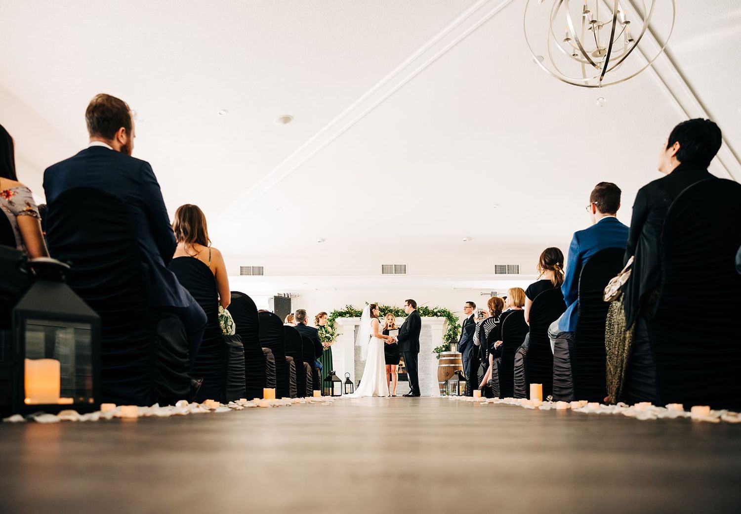Wedding ceremony aisle lined with candles and rose petals leading to couple at floral arch altar.