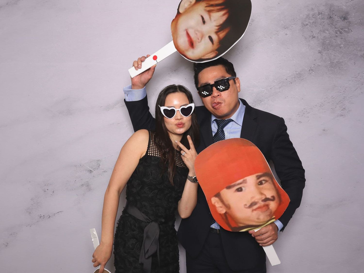 Couple posing playfully with oversized celebrity face props at a photo booth.