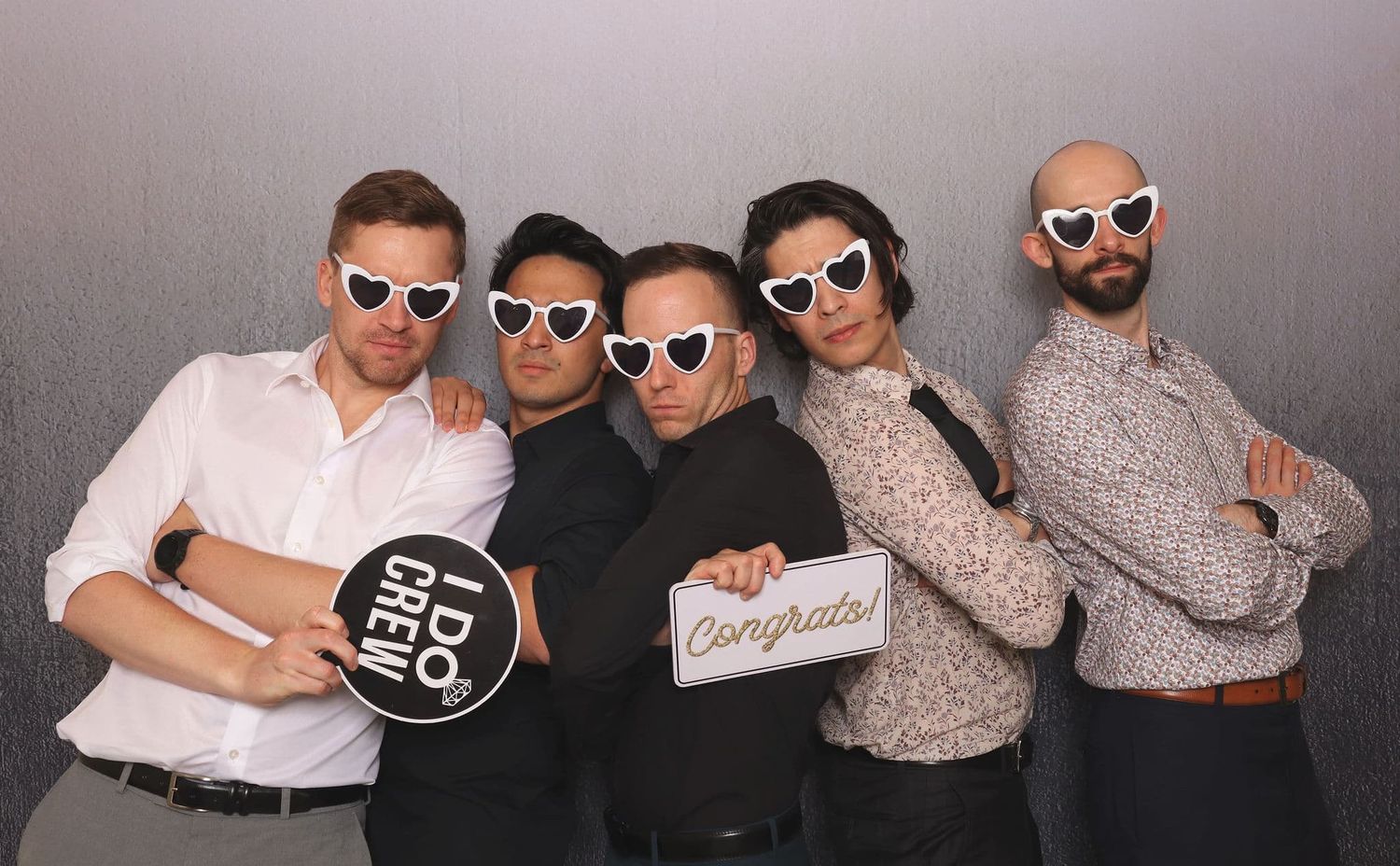 Five people wearing heart-shaped sunglasses at a party, holding Congrats signs in a fun photo booth setting.