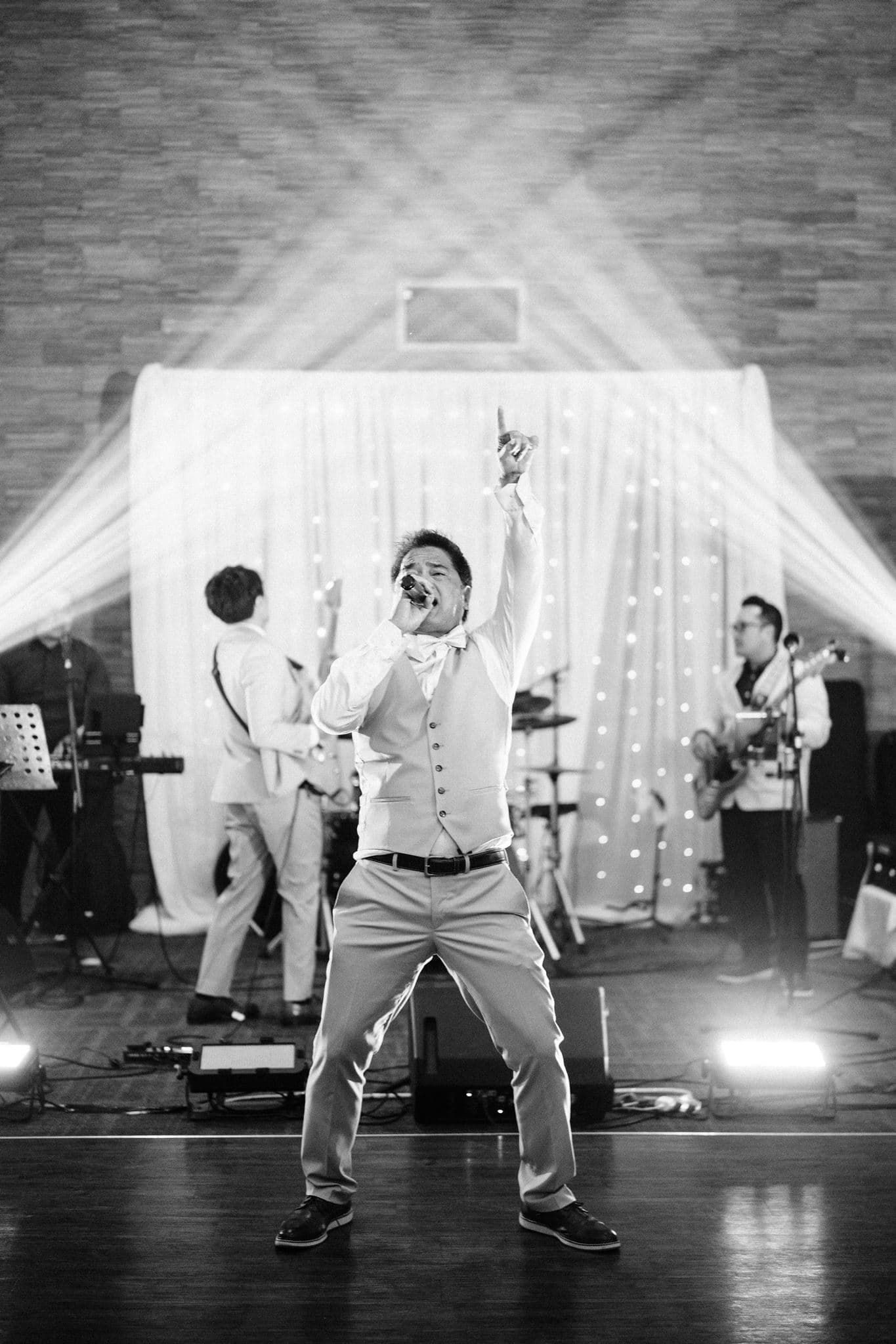Black and white photo of a groom dancing energetically at his wedding reception with a live band performing on stage.