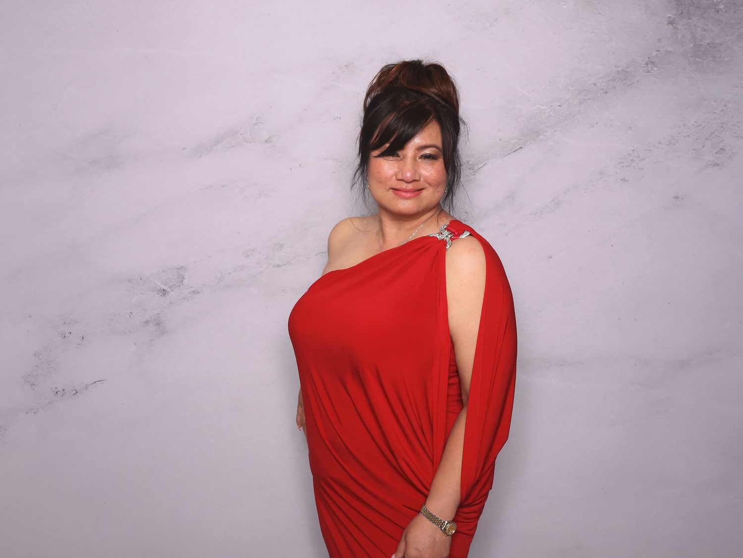 Woman in elegant red one-shoulder dress posing against a marble background.