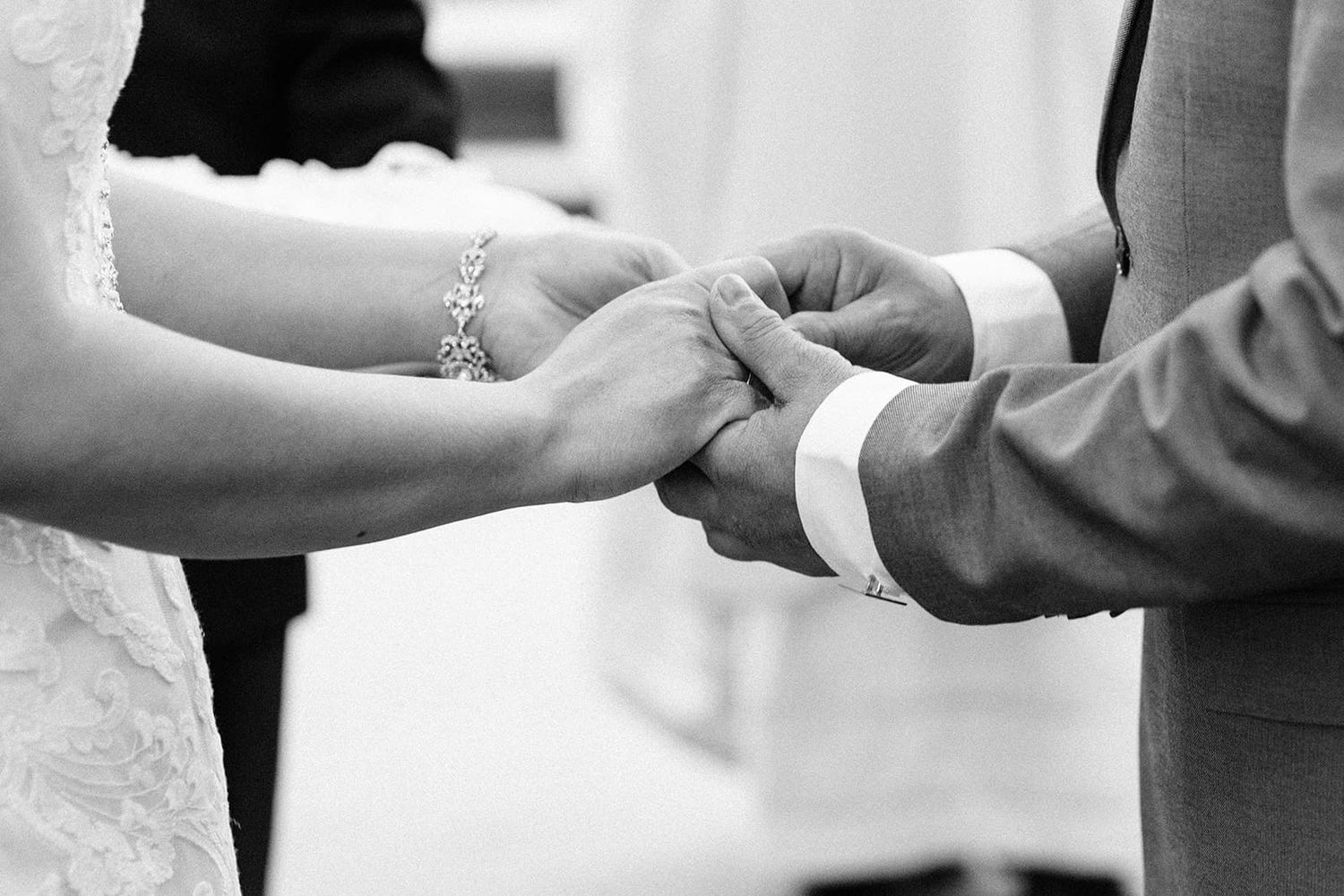 Black and white photo of a couple exchanging rings during a wedding ceremony, bride wearing a delicate bracelet.