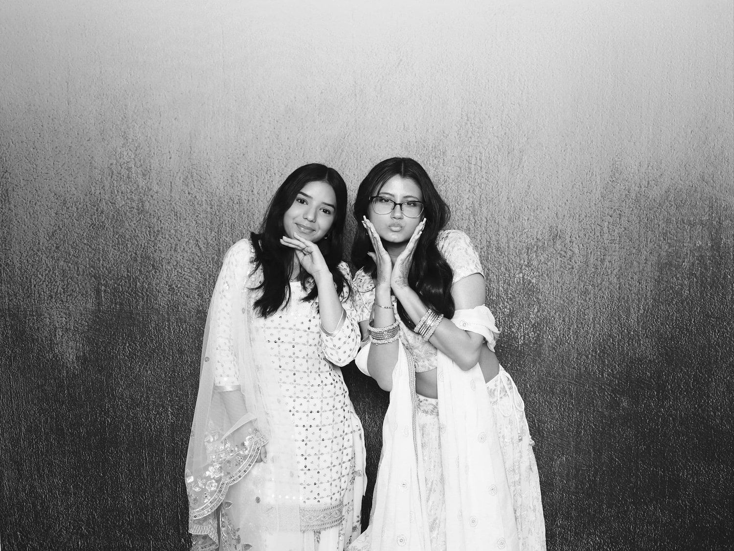 Two young women in white traditional Indian attire pose playfully in a black and white photo.