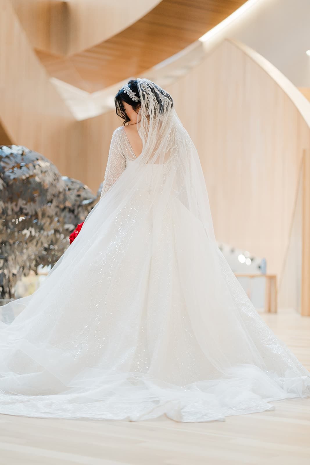 Elegant bride in a stunning white lace wedding gown with long veil and cathedral train viewed from behind.