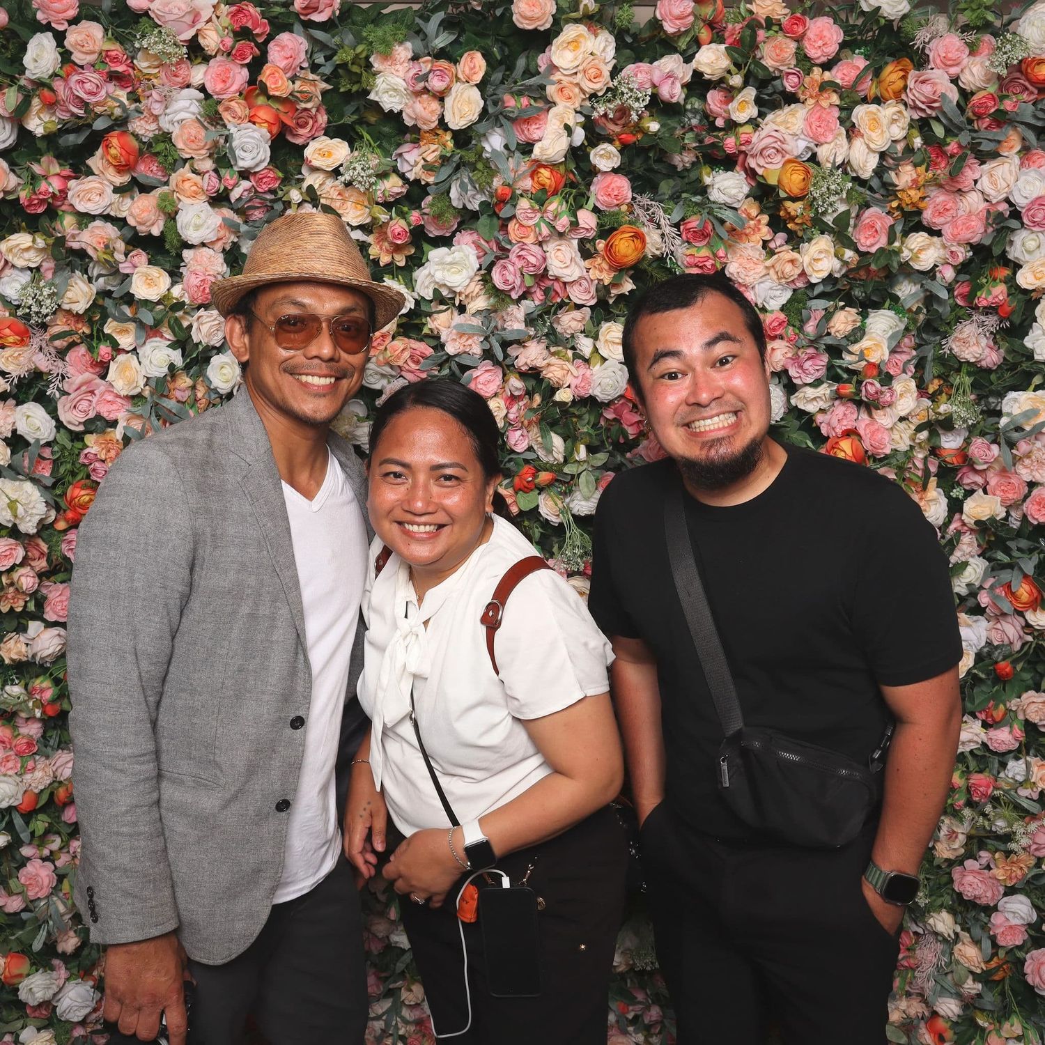 Three friends smiling together in front of a vibrant floral wall backdrop.
