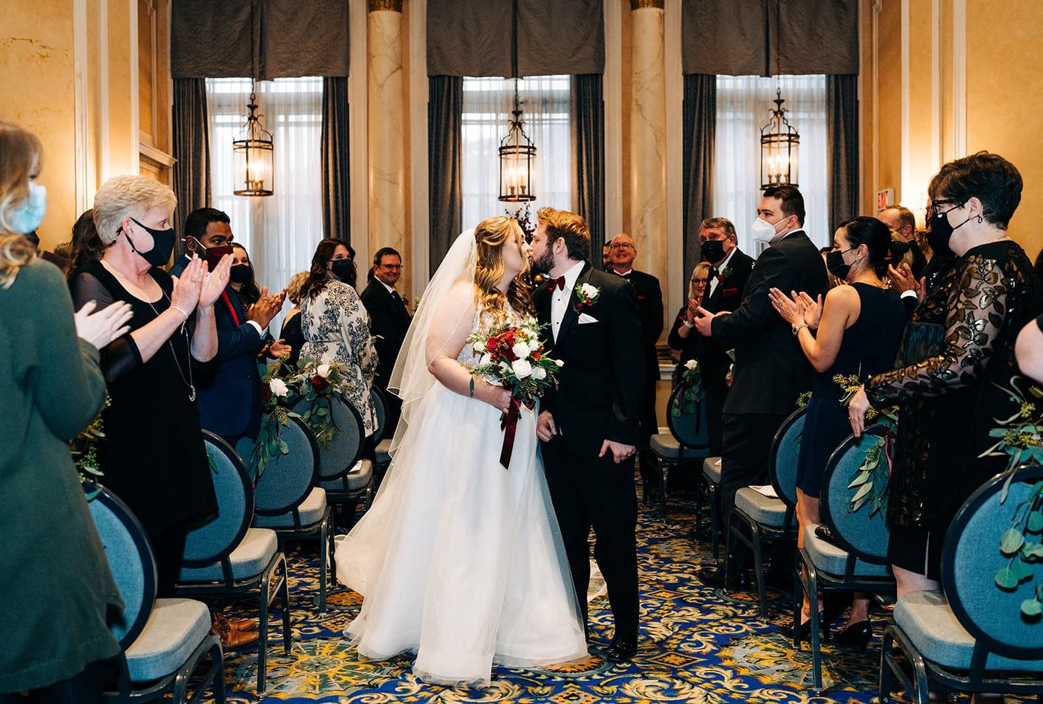 Newlyweds sharing a kiss while walking down the aisle at their indoor wedding ceremony.