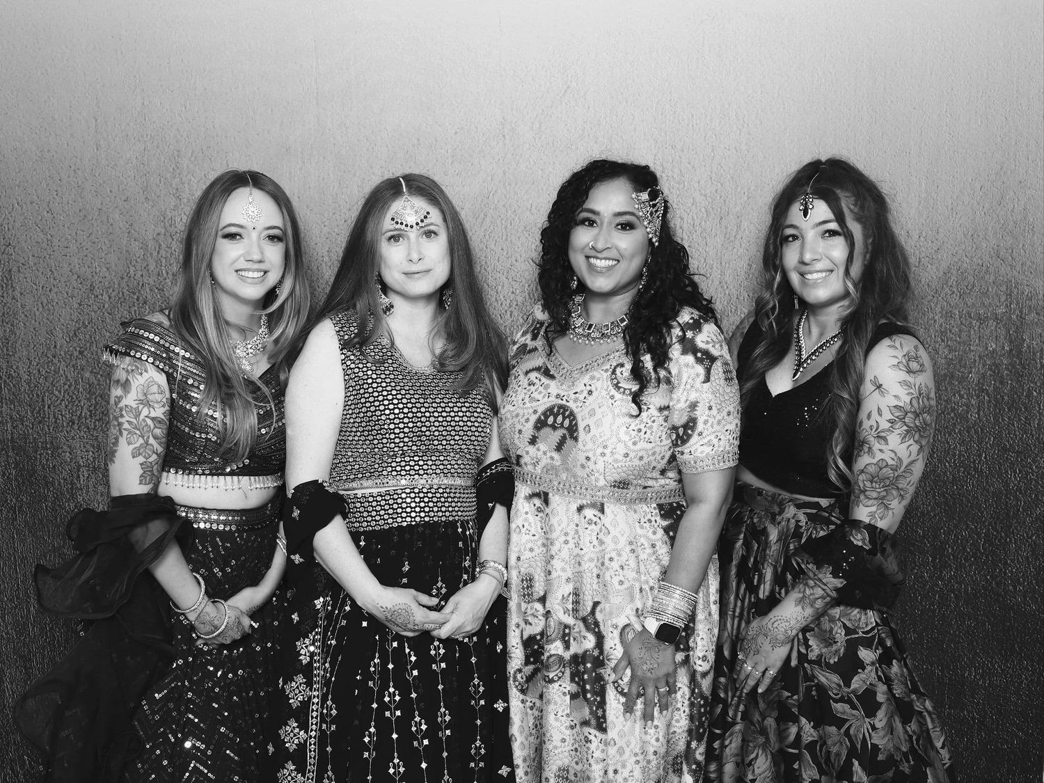 Black and white photo of four women in elegant Indian attire posing together.