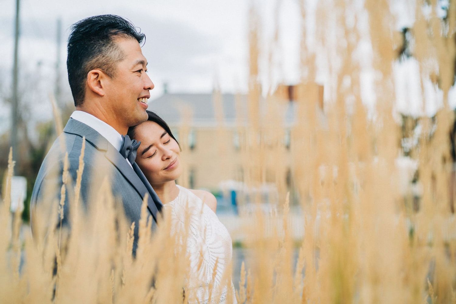 Couple sharing a romantic moment among golden tall grasses, woman resting head on mans shoulder outdoors.