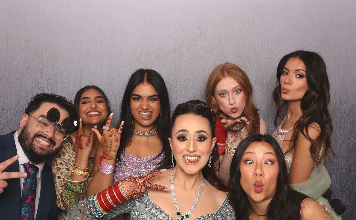 Group of seven friends posing playfully in a photo booth at a wedding celebration.