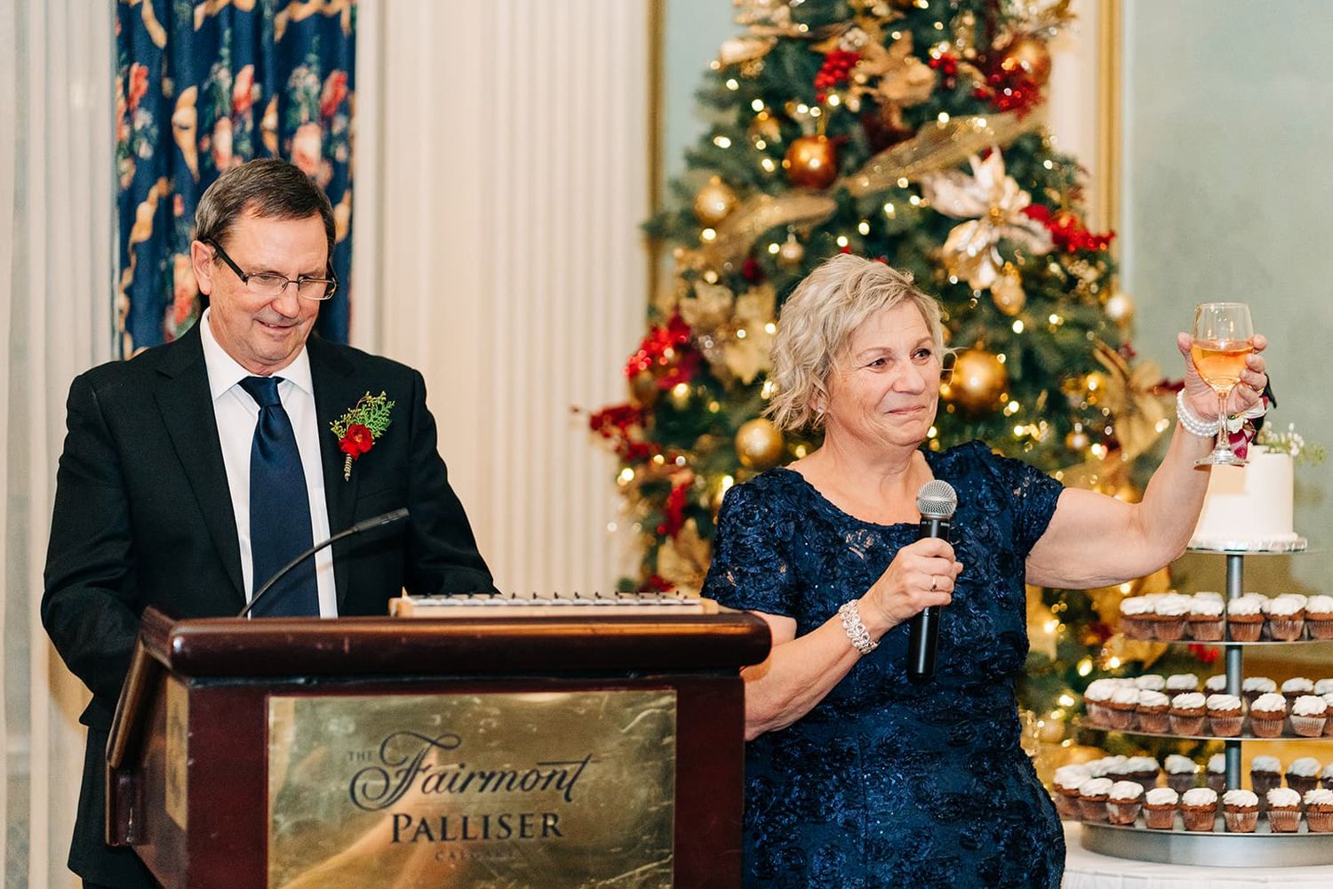 Couple giving a toast at Fairmont Palliser holiday wedding reception with Christmas tree in background.