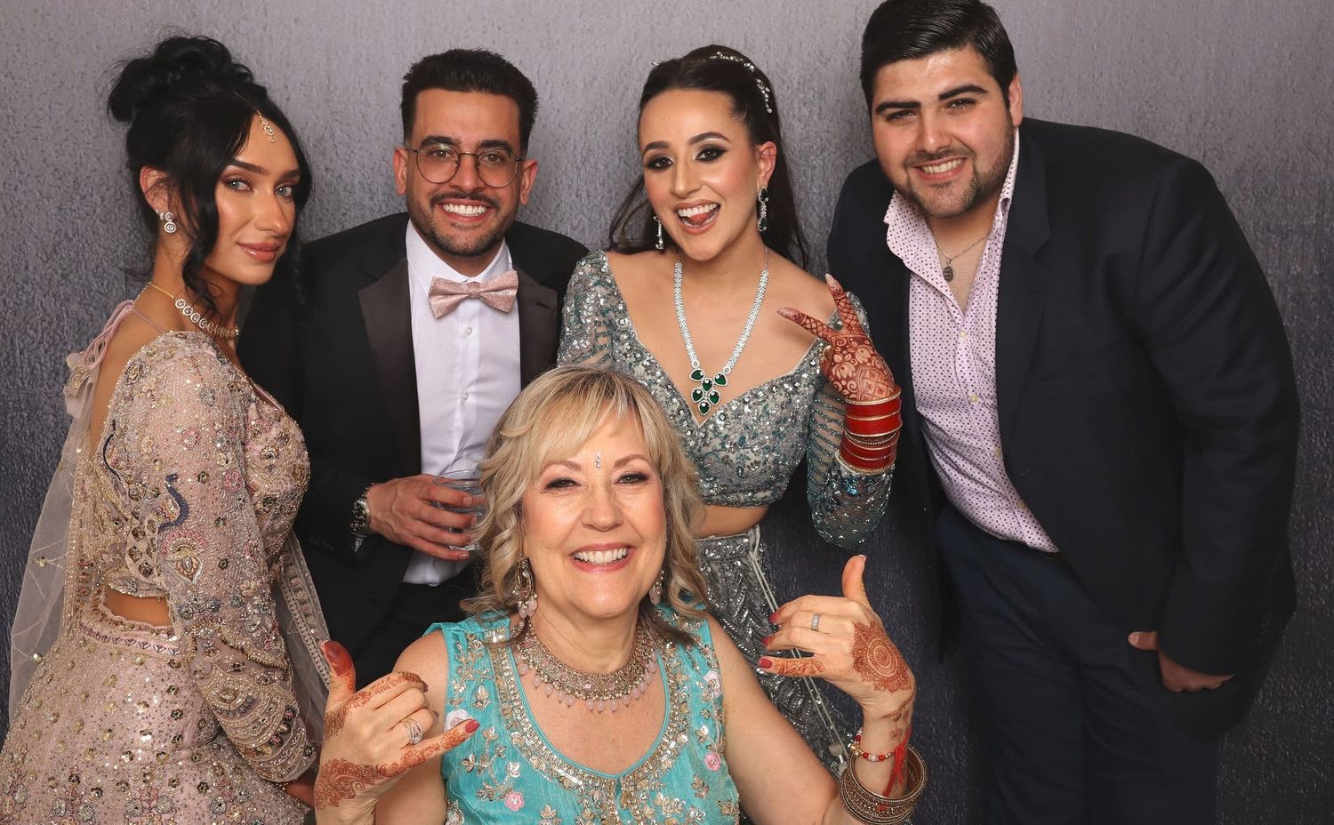 Five people posing together at a formal event, with a woman in teal giving thumbs up and others in elegant attire.