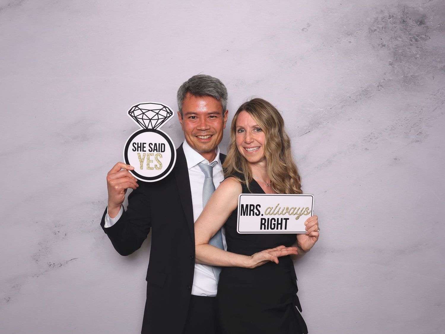 Couple poses with wedding signs including She Said Yes and Mrs. Always Right at photo booth.