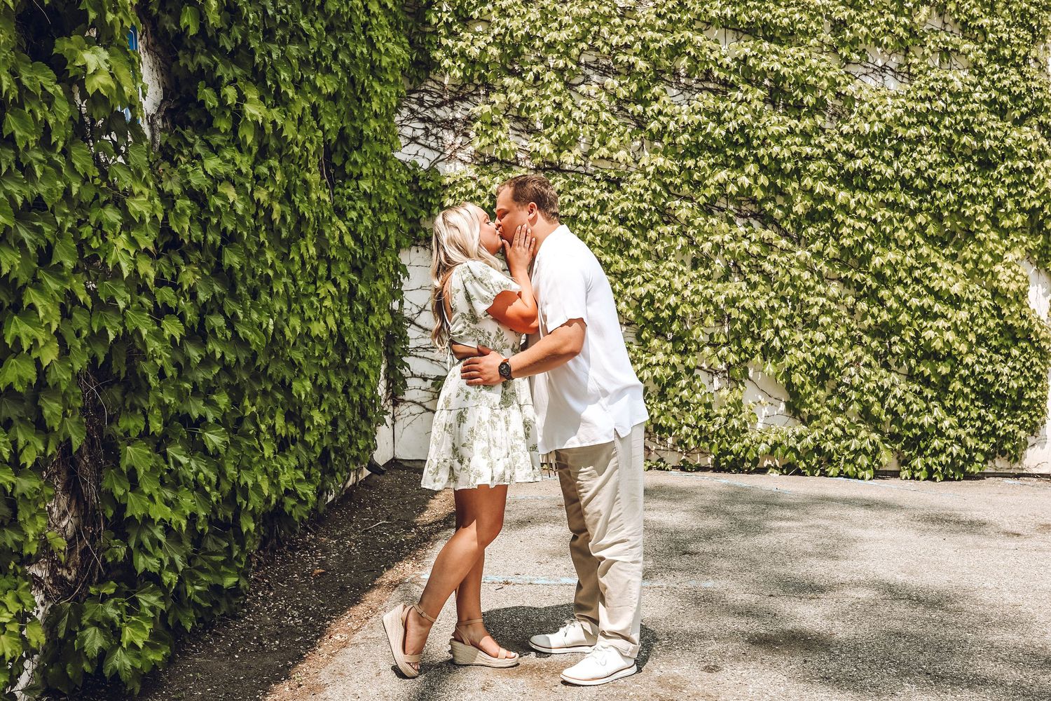 A romantic embrace against an ivy-covered wall on a sunny day.