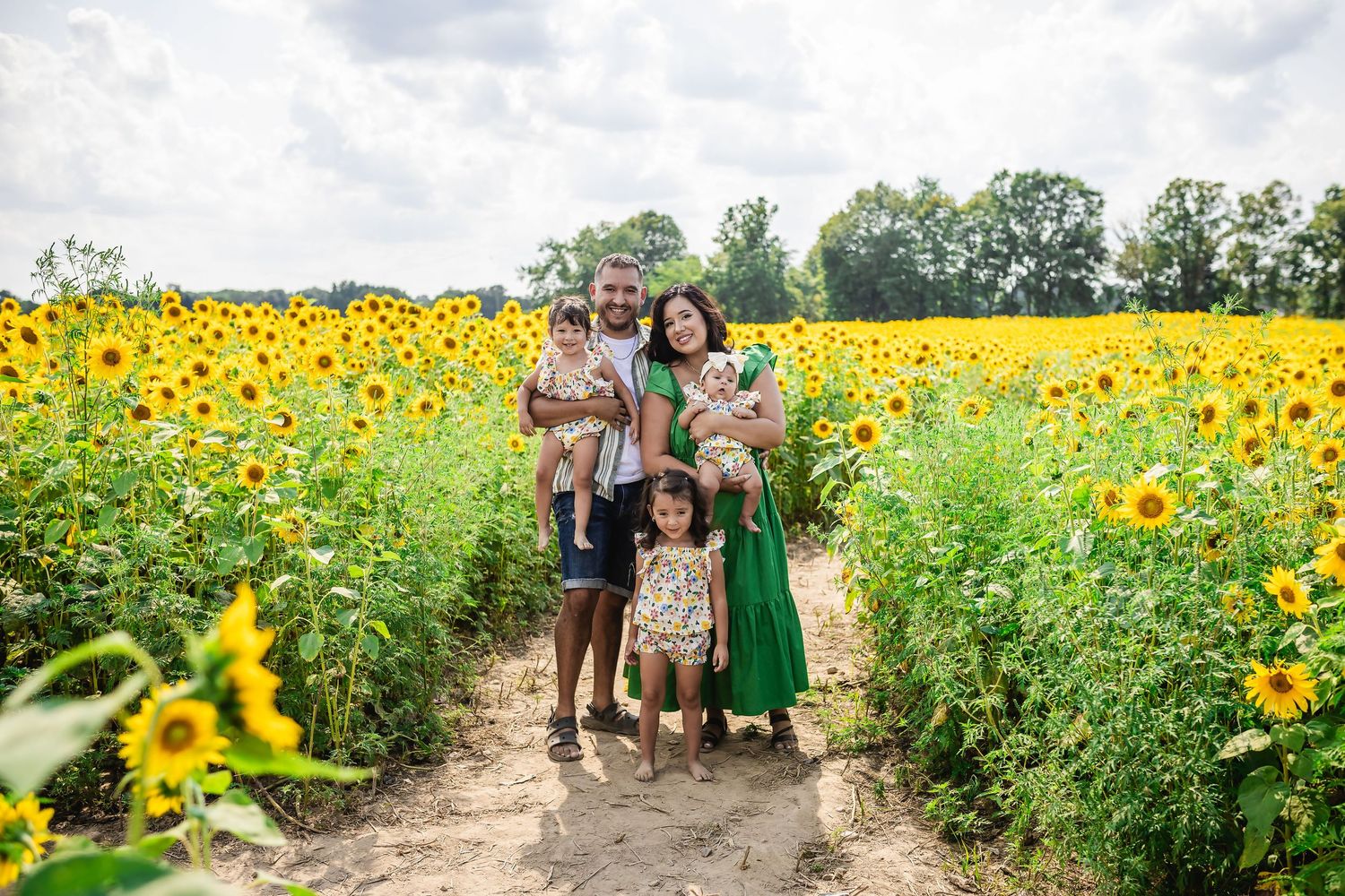 Family of five posing happily in a vibrant sunflower field on a sunny day.