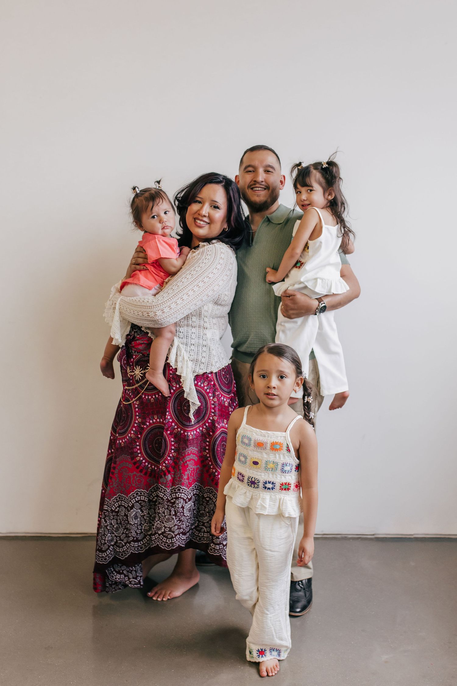 A joyful family of five poses together, parents holding two toddlers while an older child stands in front.