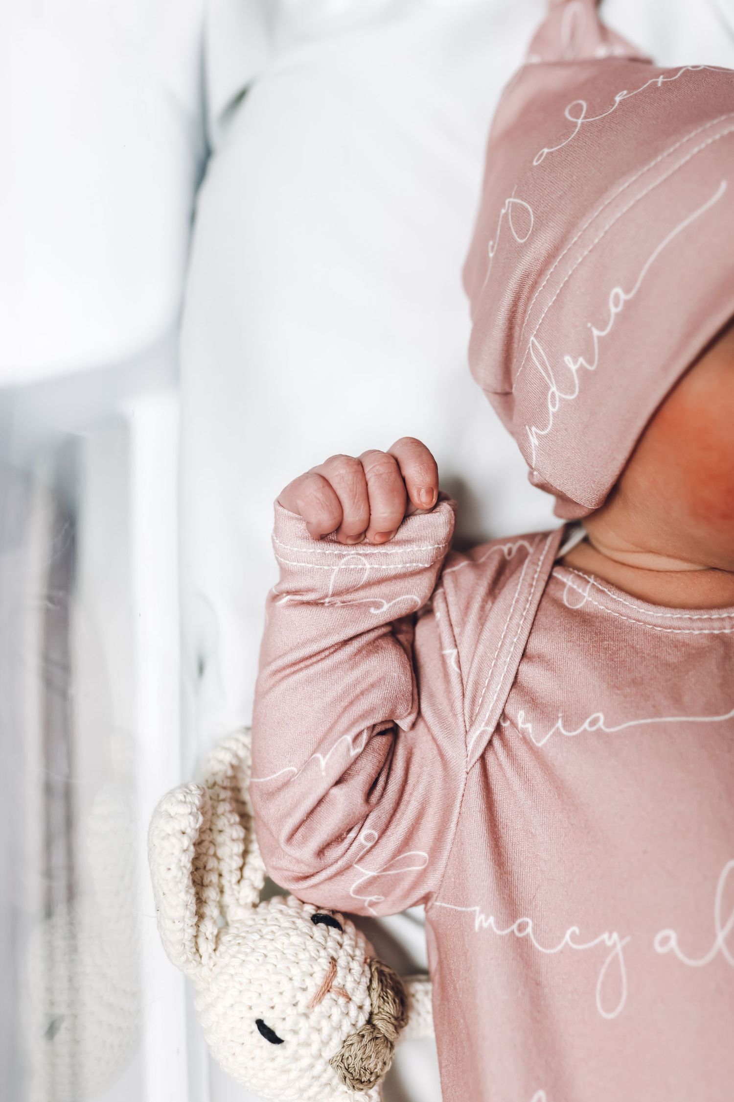 Close-up of baby's hand holding plush toy in pink clothing.