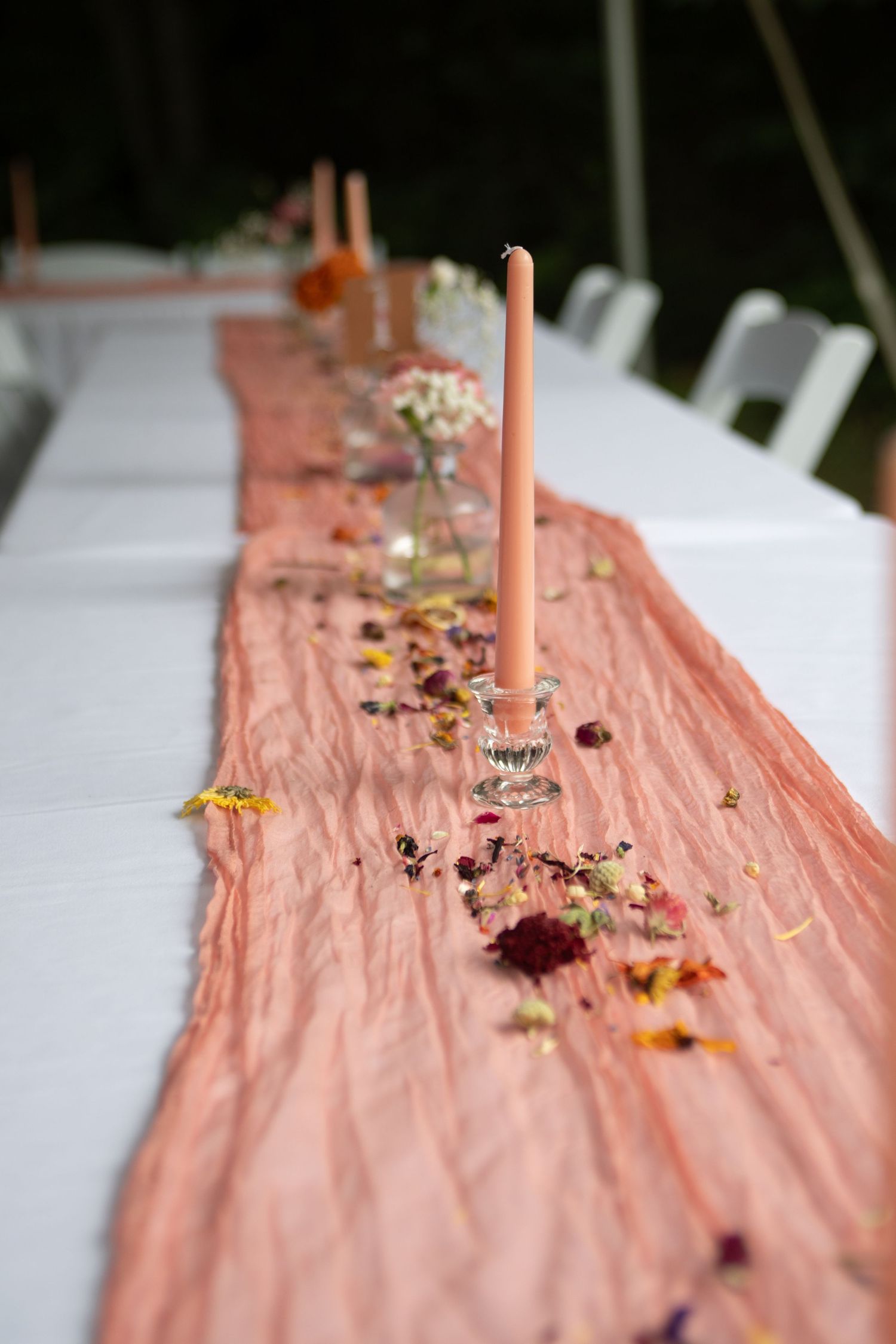 Peach-colored table runner decorated with scattered flower petals and coral taper candles.