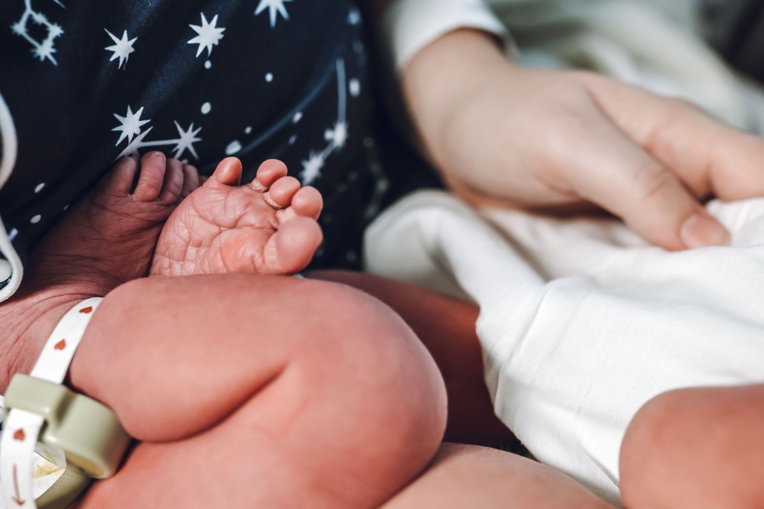 Close-up of newborn baby tiny feet with hospital ID bracelet resting on caregiver's lap.