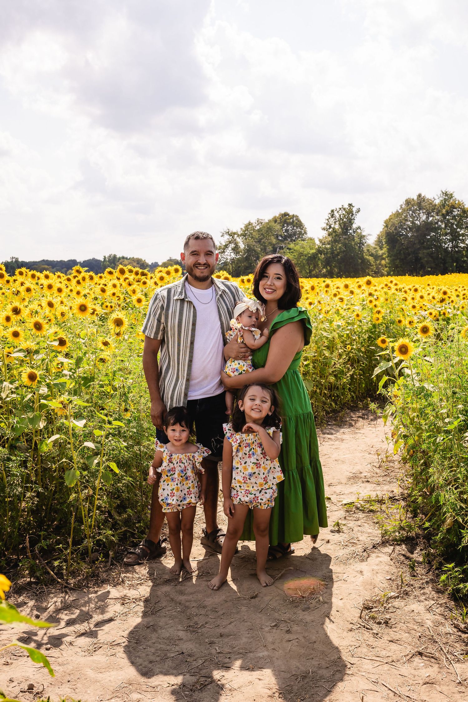 A family stands together in a vibrant field of blooming sunflowers on a sunny summer day.