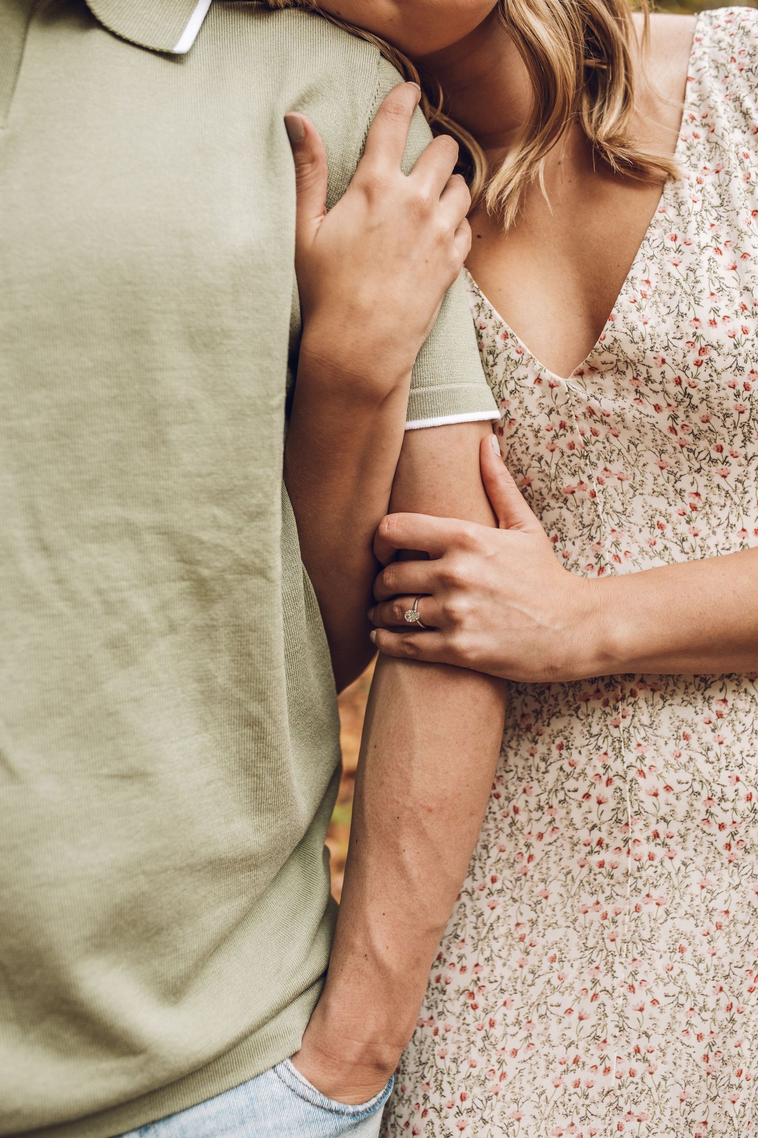 Close-up shot of couple embracing, wearing sage green t-shirt and floral summer dress.
