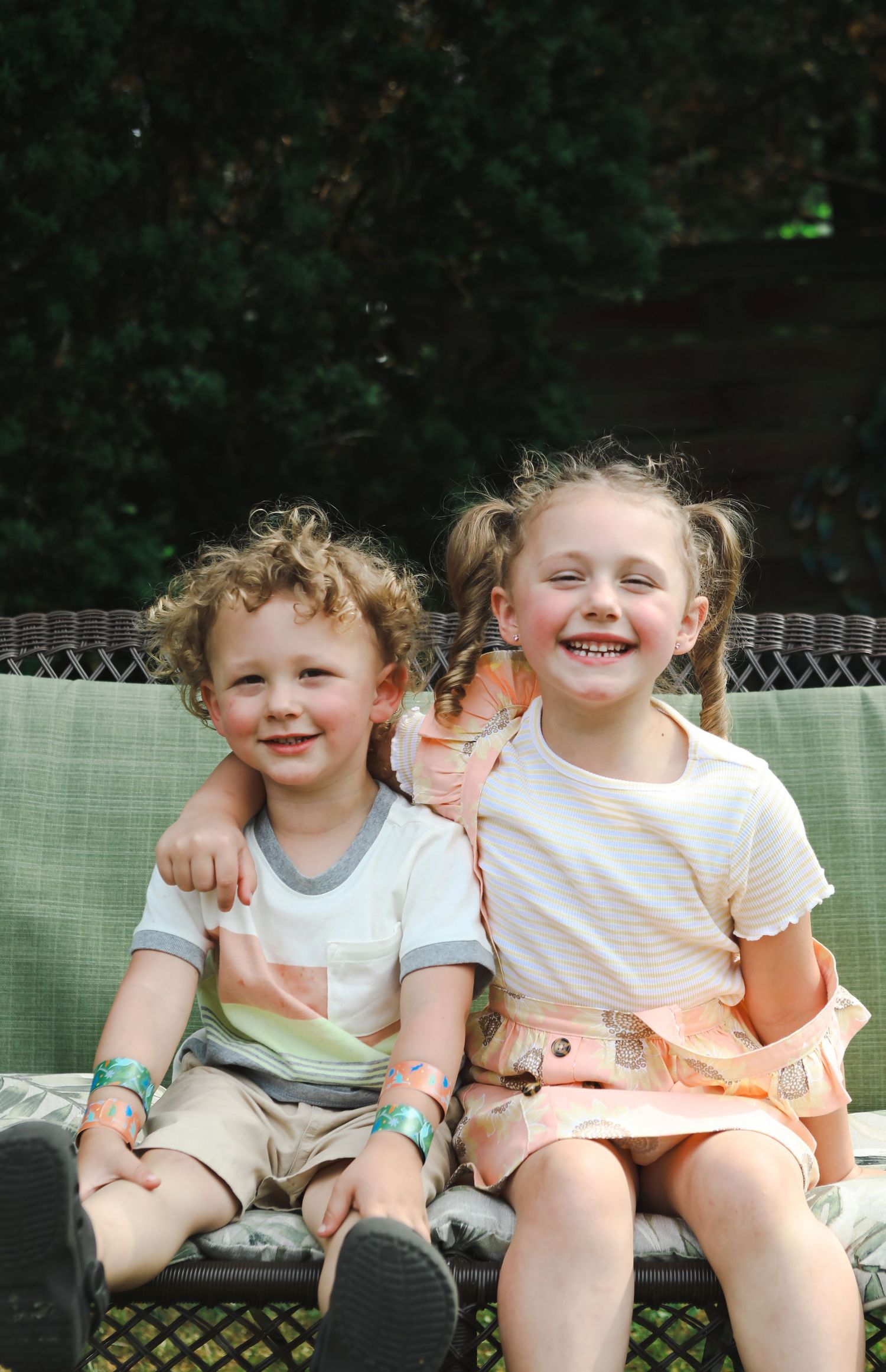 Young children sitting together and laughing on outdoor furniture.
