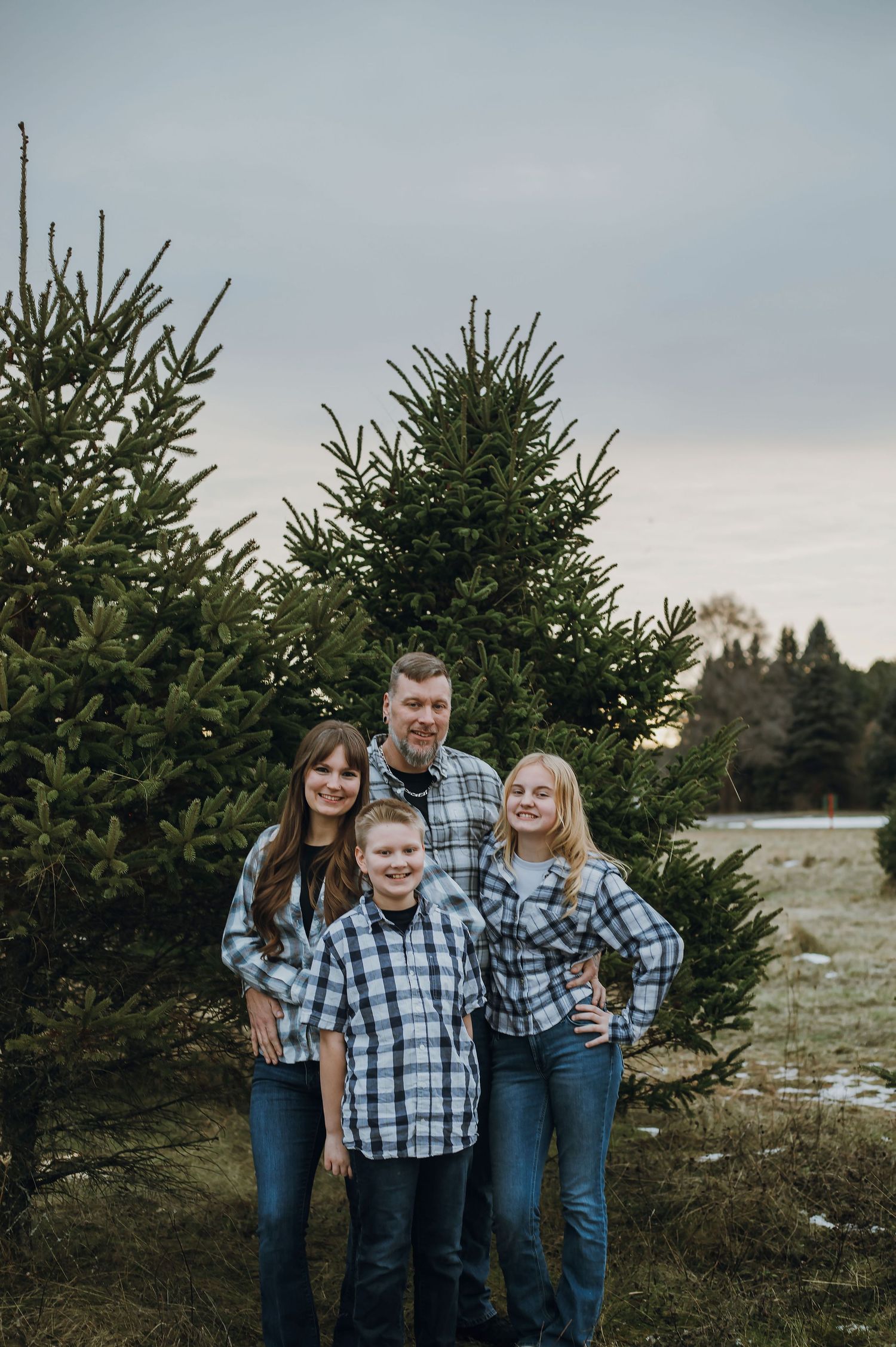 Winter family portrait taken in front of evergreen trees at dusk.