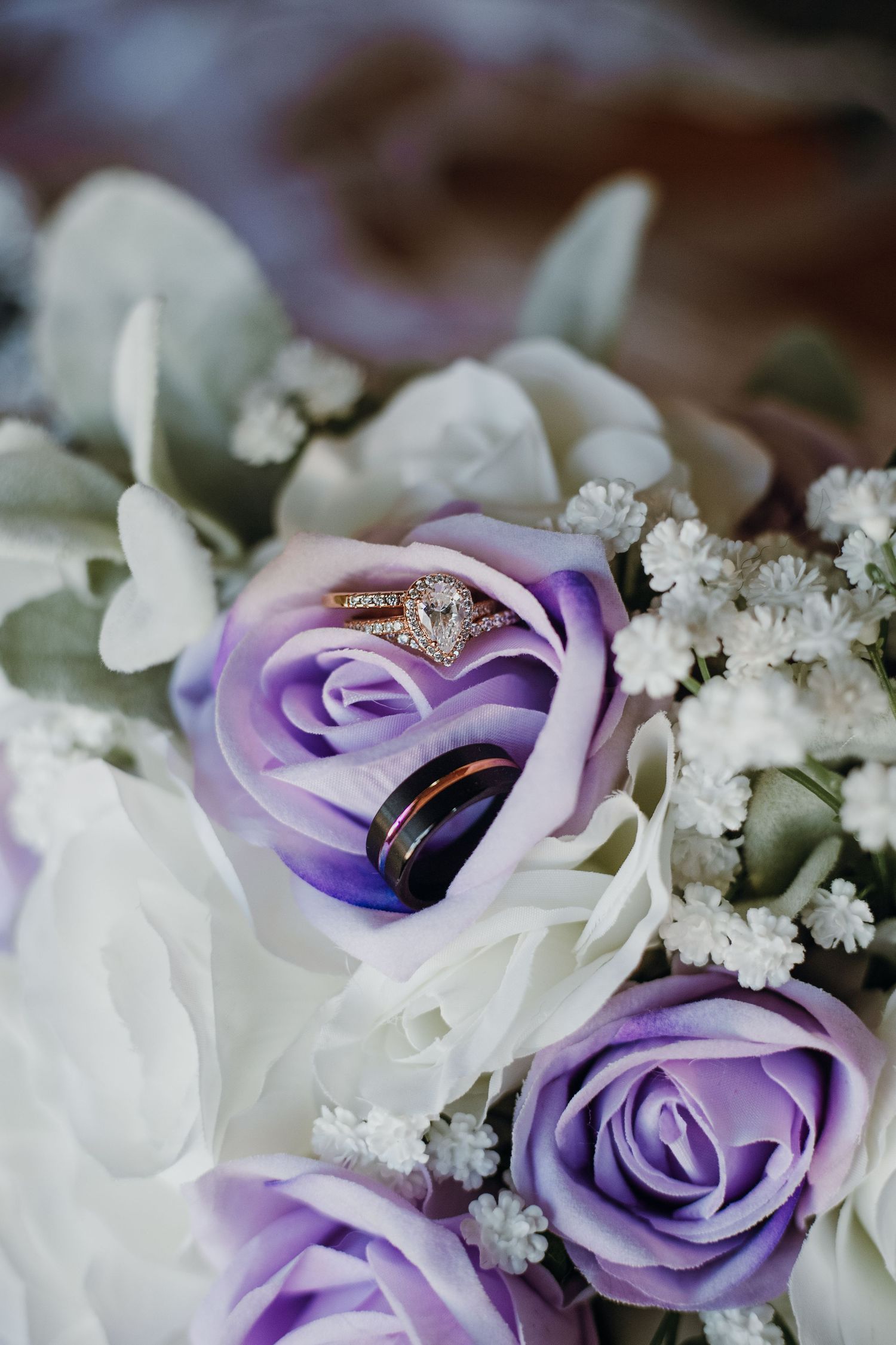 Wedding rings nestled among purple and white roses with delicate floral accents.