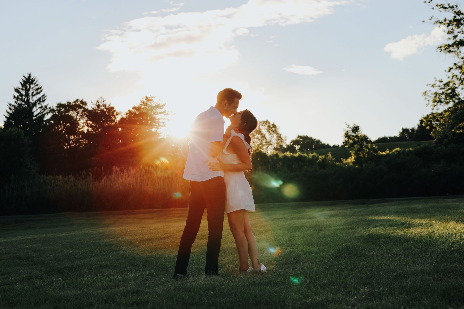 A couple embraces in a grassy field during golden hour sunset.