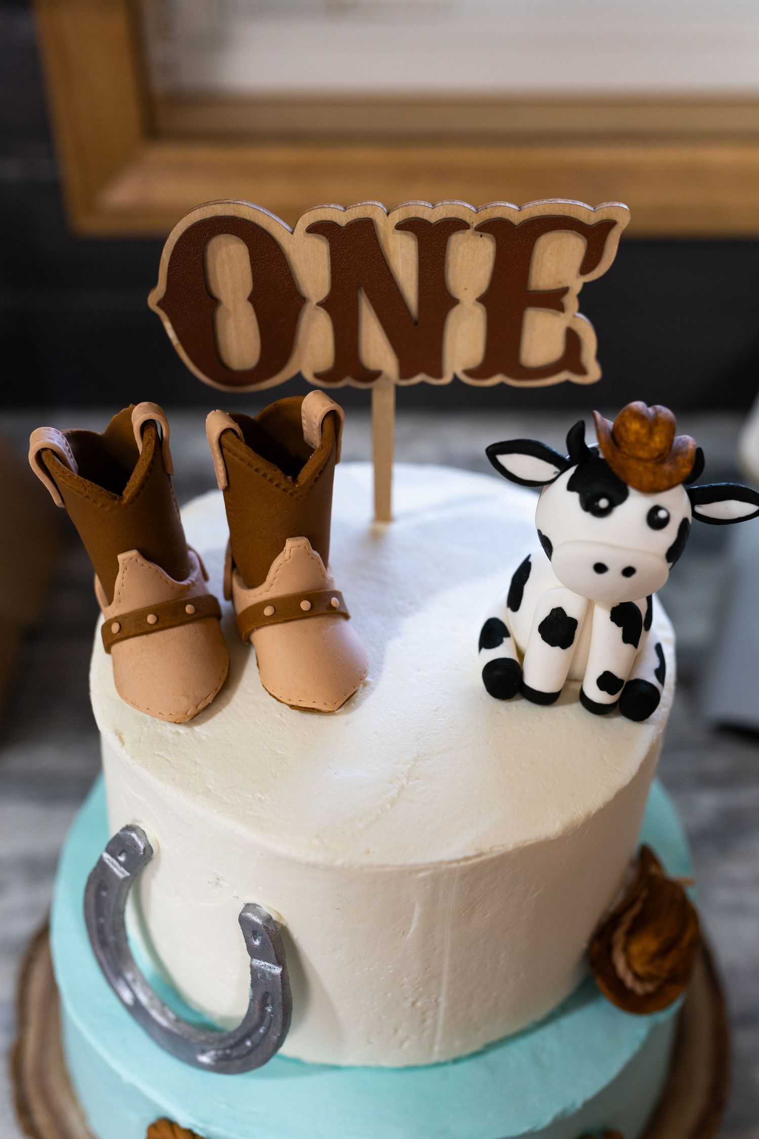 Western cowboy first birthday cake with ONE topper, mini boots, horseshoe, and fondant cow wearing a hat.