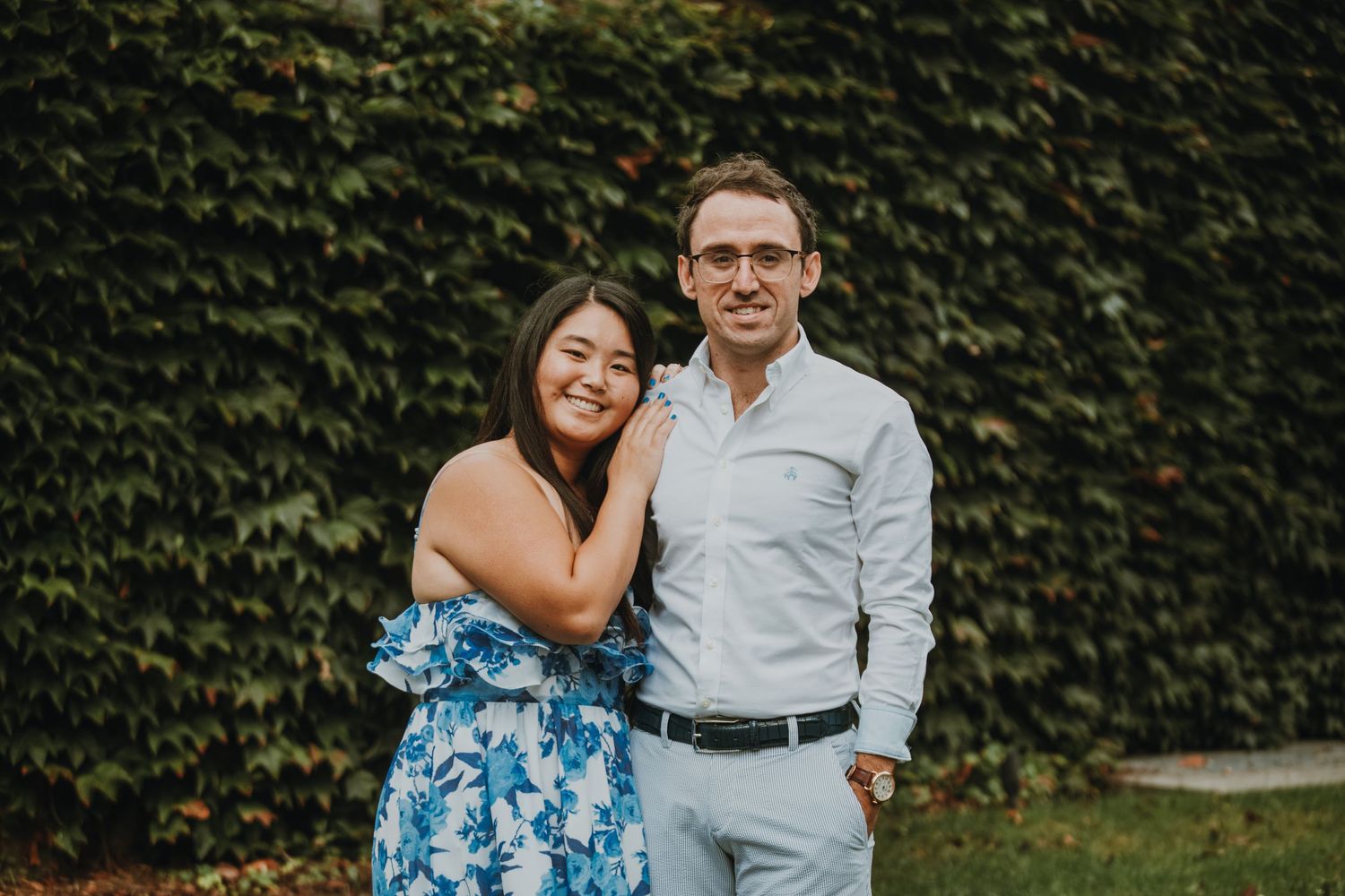 A couple poses together against a wall covered in lush green ivy.