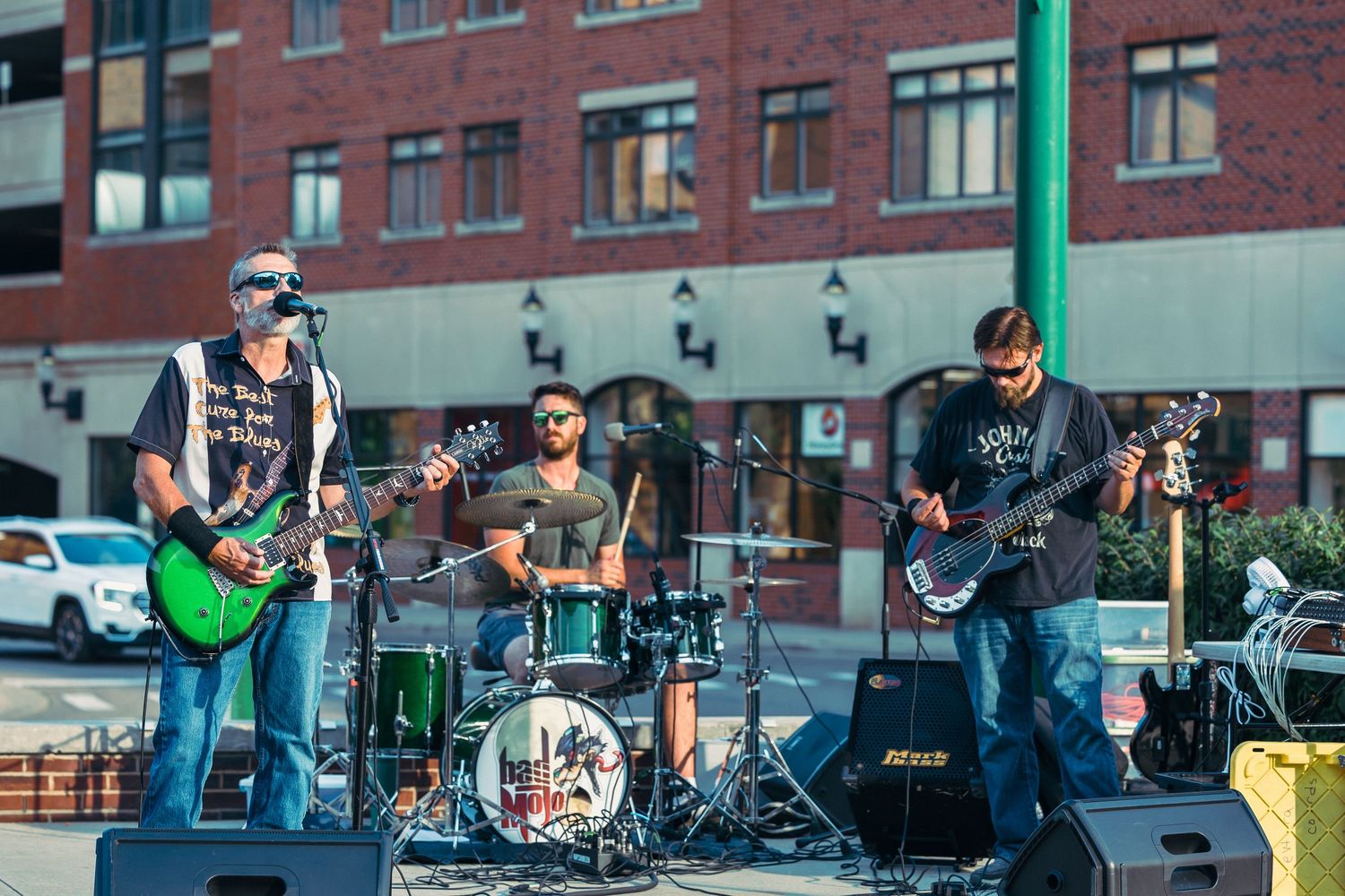 Outdoor rock band performing on a city street stage with guitars and drums on a sunny day.