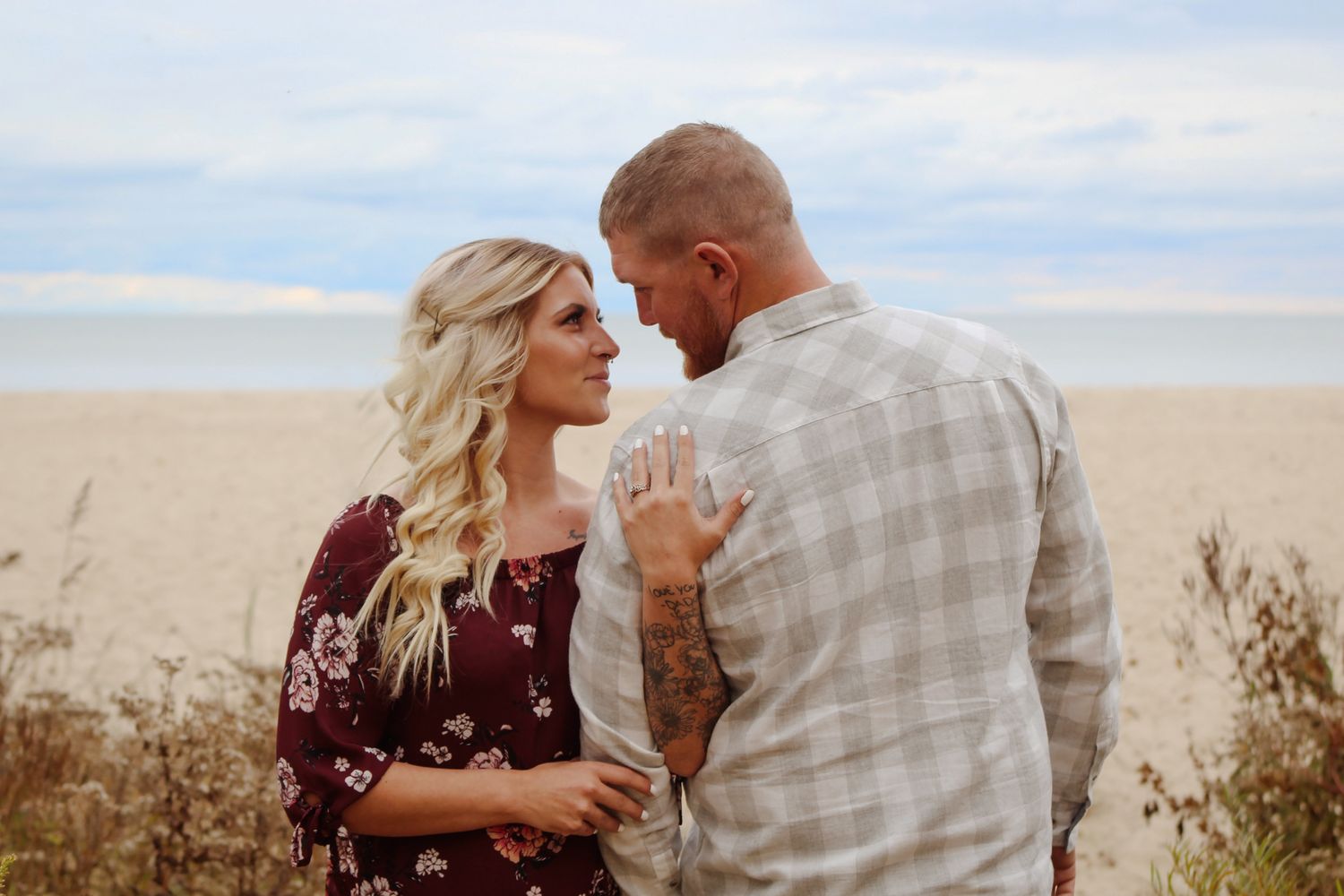 A couple shares an intimate moment on an open field against a cloudy sky.
