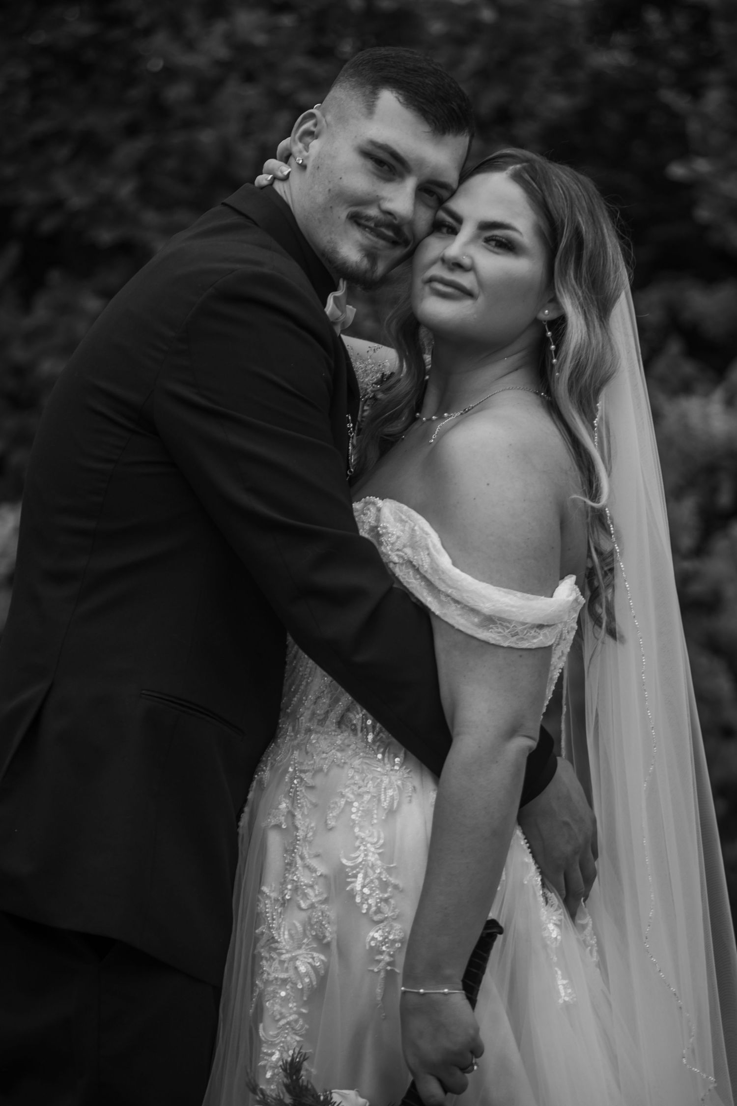 A black and white wedding portrait showing a tender moment between newlyweds, with the bride wearing a lace gown and veil.